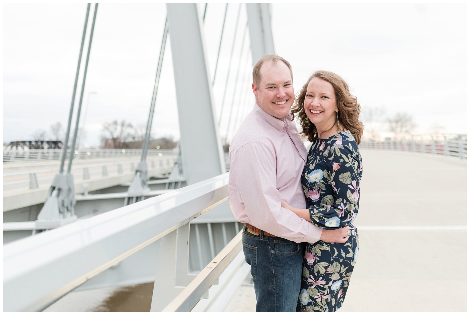 an outdoor spring engagement session with an engaged couple laughing and looking at the camera while standing on a bridge at sunset Scioto Mile Engagement Session Columbus, Ohio