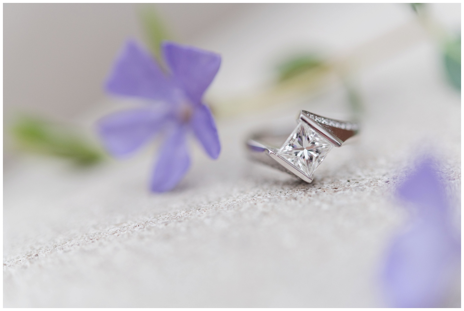 a solitaire engagement ring surrounded by purple spring flowers on concrete 