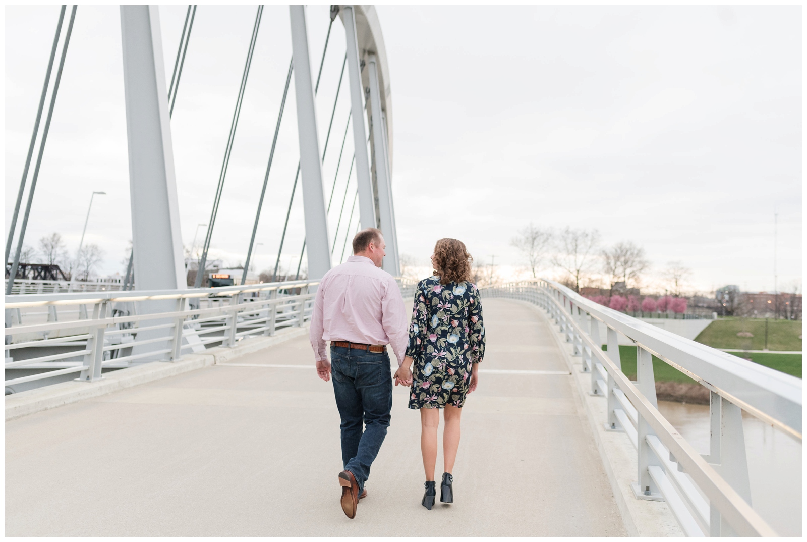an engaged couple walks away from the camera on a bridge at sunset on the scioto mile in downtown columbus, ohio 