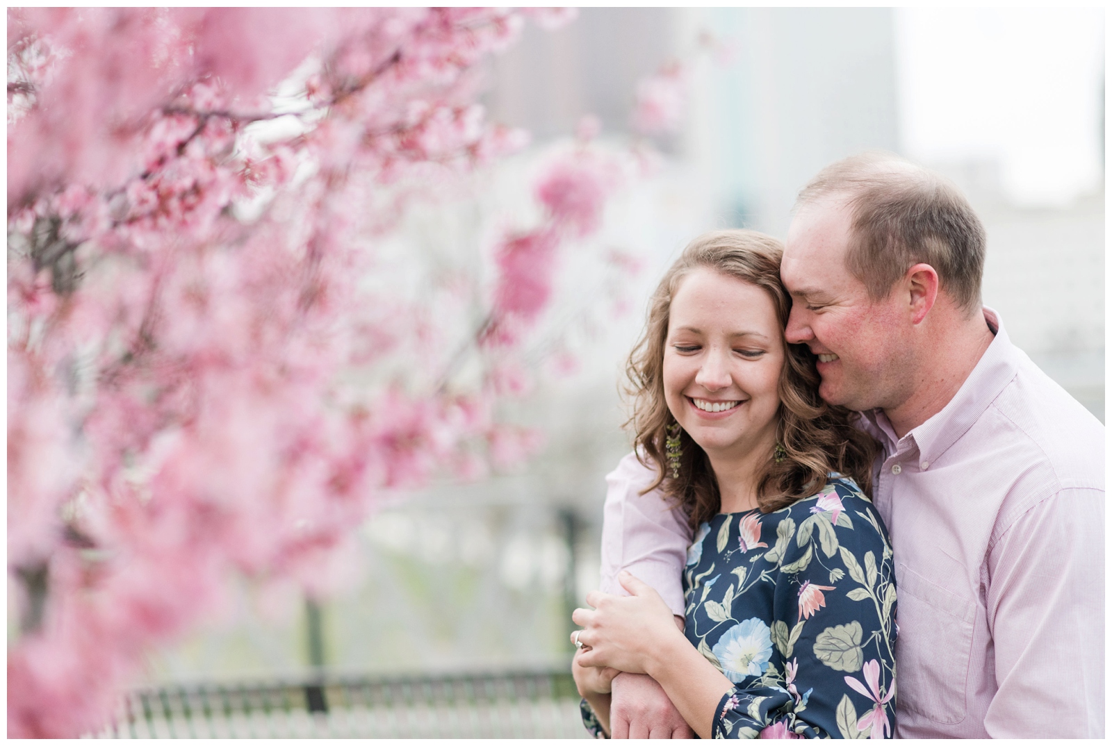 romantic spring engagement sessions at scioto mile with redbud trees blooming and the bride in an navy and pink floral dress and the groom in a pink button down shirt 