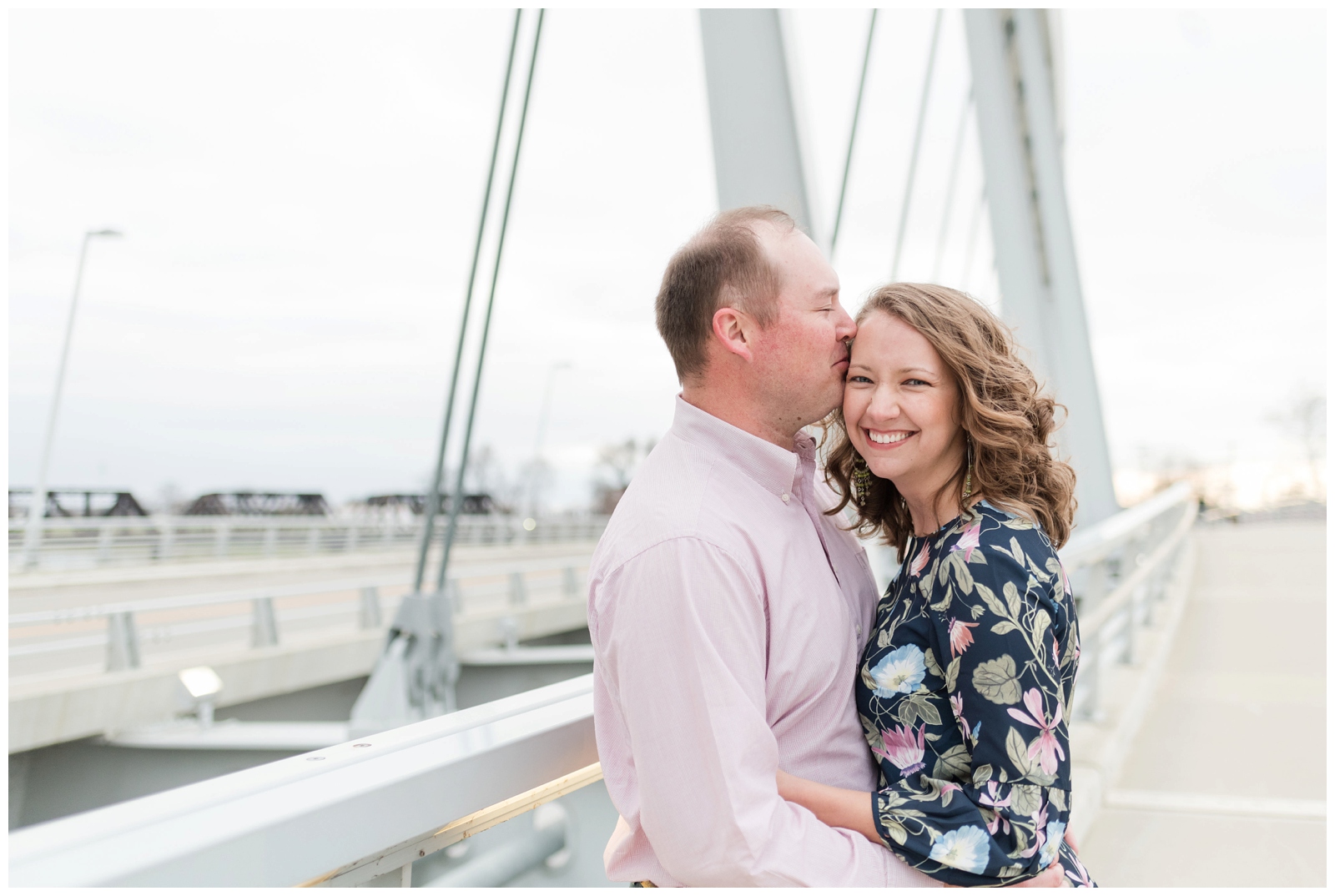 groom is kissing his engaged bride on a bridge in spring in downtown coumbus ohio on the scioto mile 