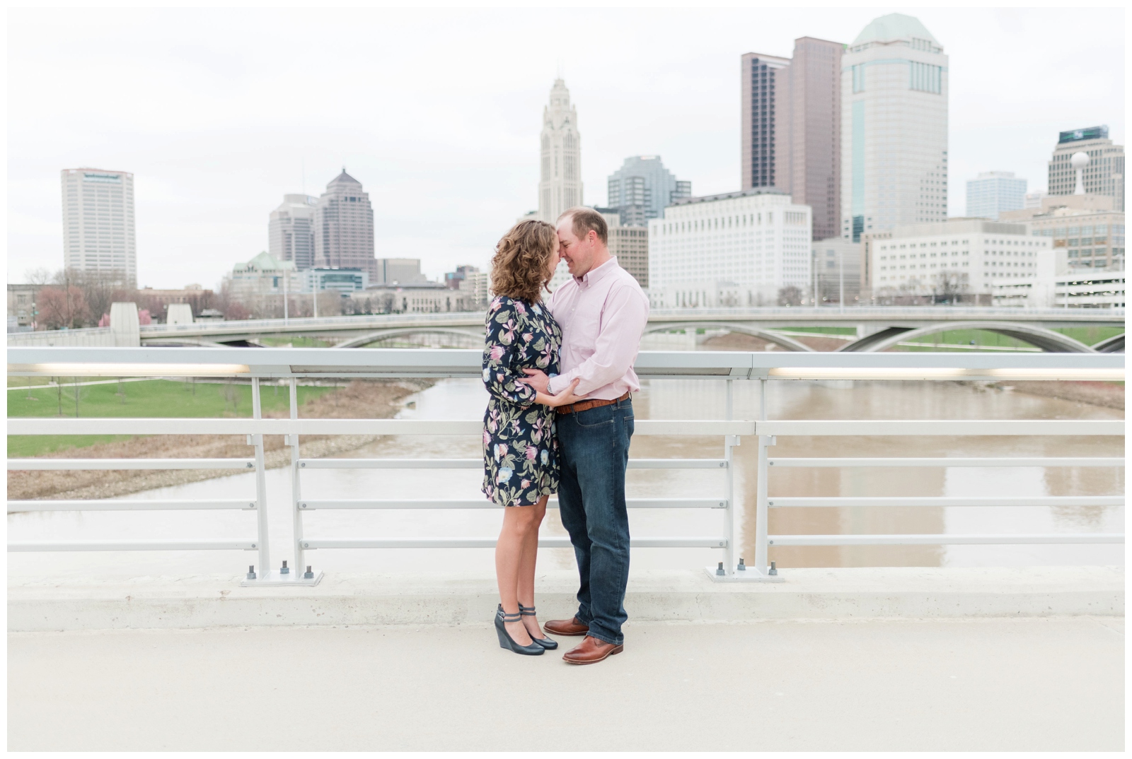 engaged couple embraces with a city scene behind them of Columbus, Ohio at Scioto Mile 