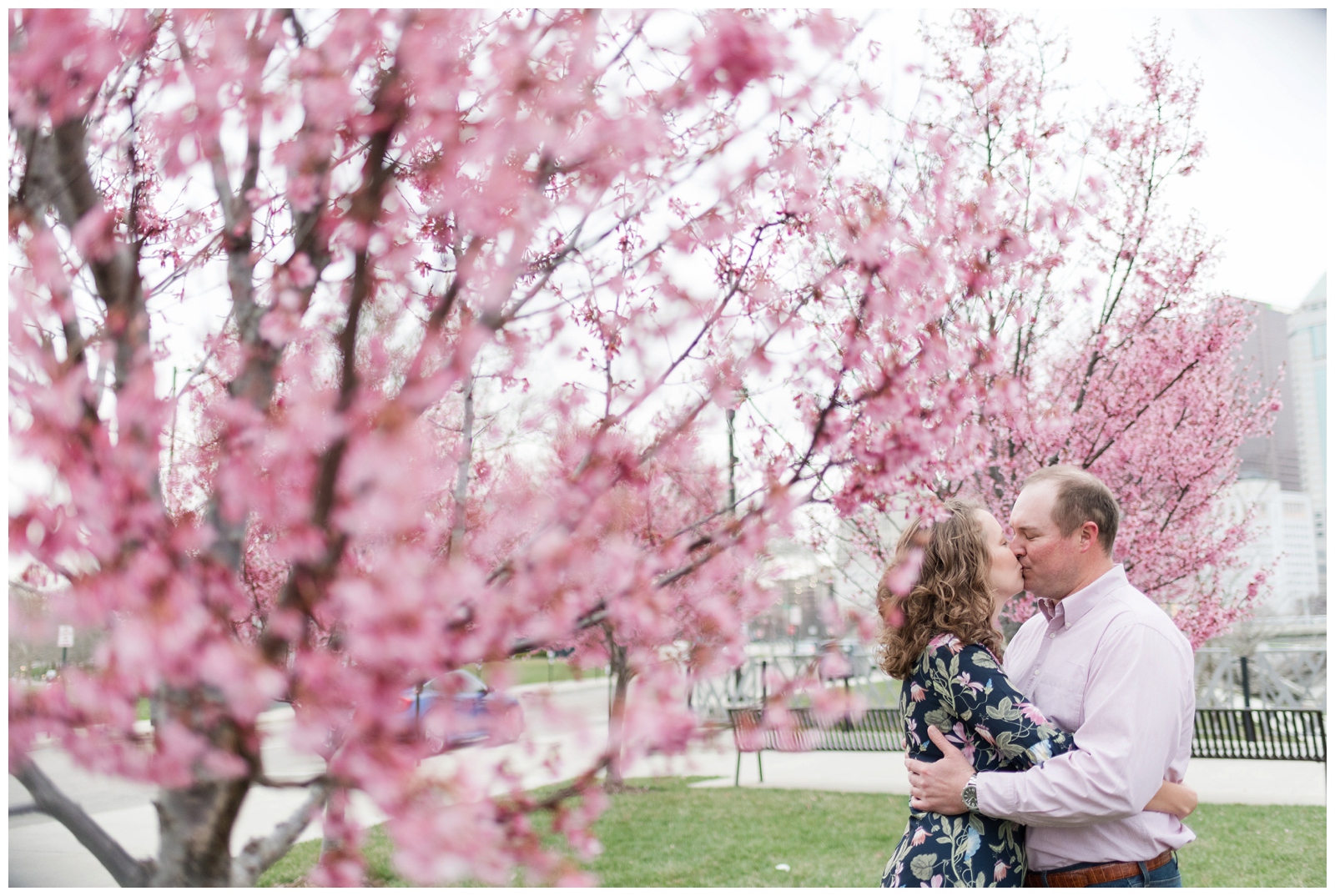 a romantic engagement session in downtown columbus with a happy couple kissing each other surrounding by pink spring blossoms 