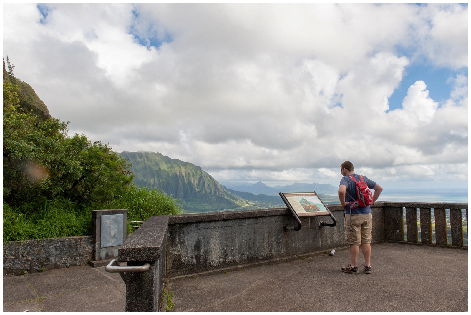 man standing and reading about the battles and more information on the lookout at Looking out to the ocean from Pali Lookout with the cliff and bees on Oahu hawaii