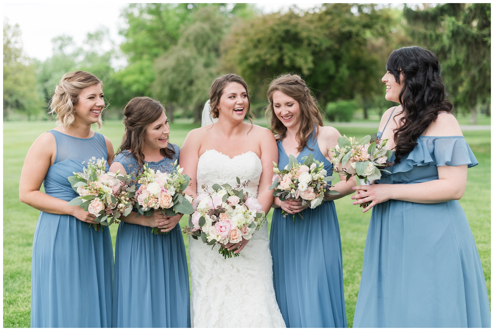 bride laughs with four bridesmaids in blue gowns on wedding day