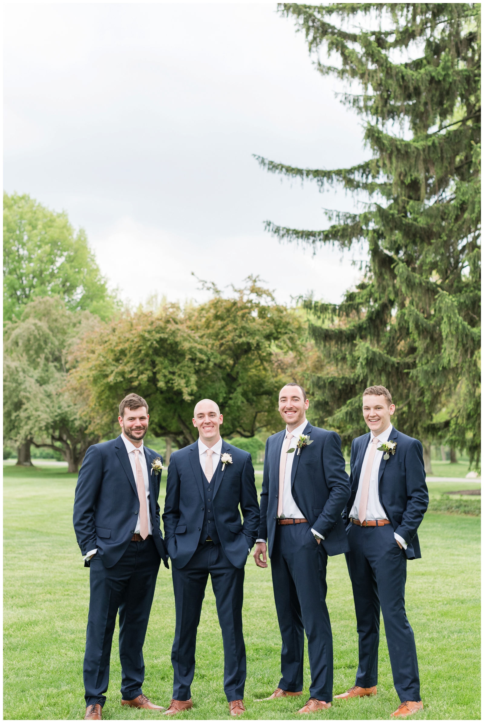 groom and three groomsmen in navy suits with tan shoes laugh at Brookside Golf and Country Club