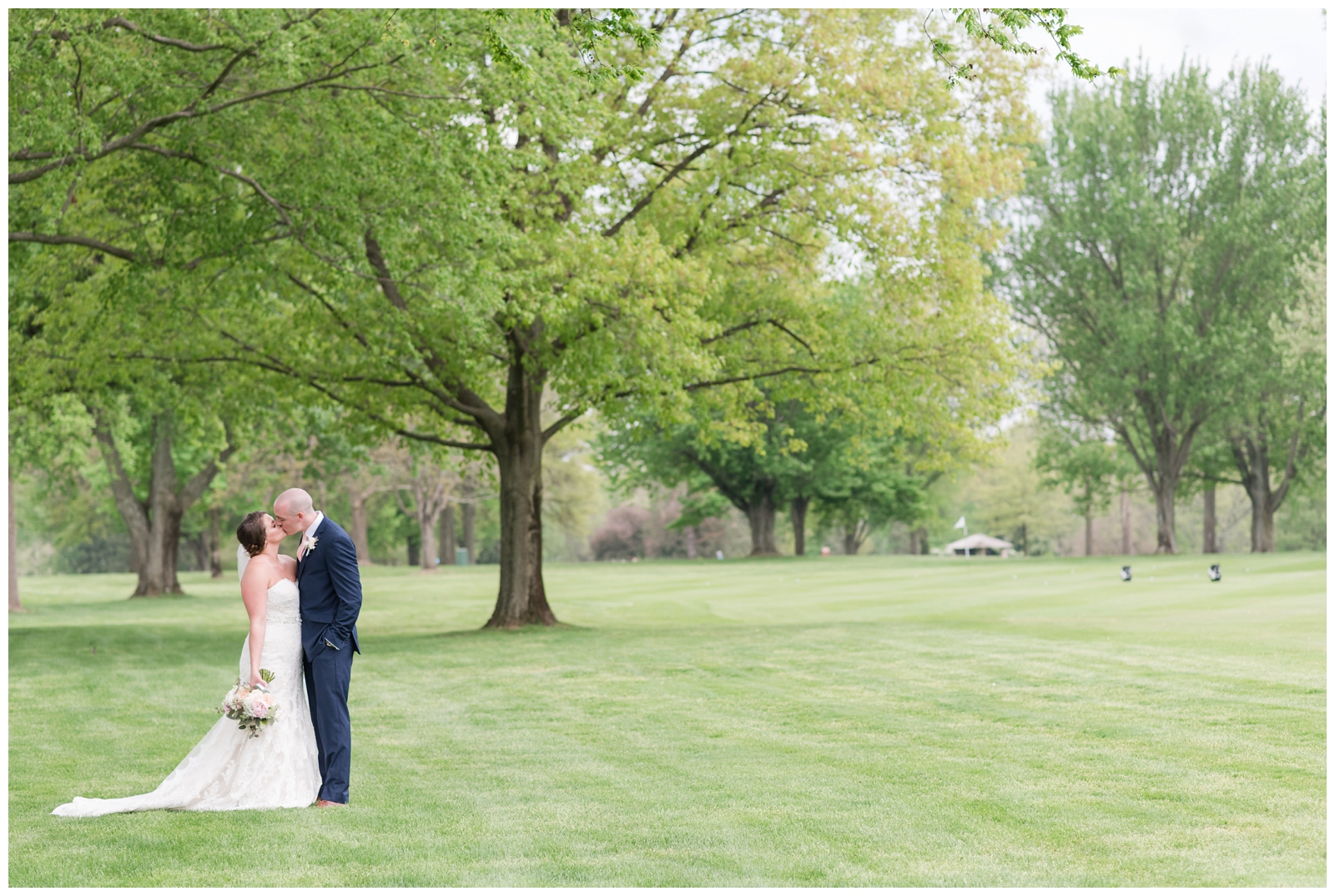 bride and groom kiss under trees on green of Brookside Golf and Country Club