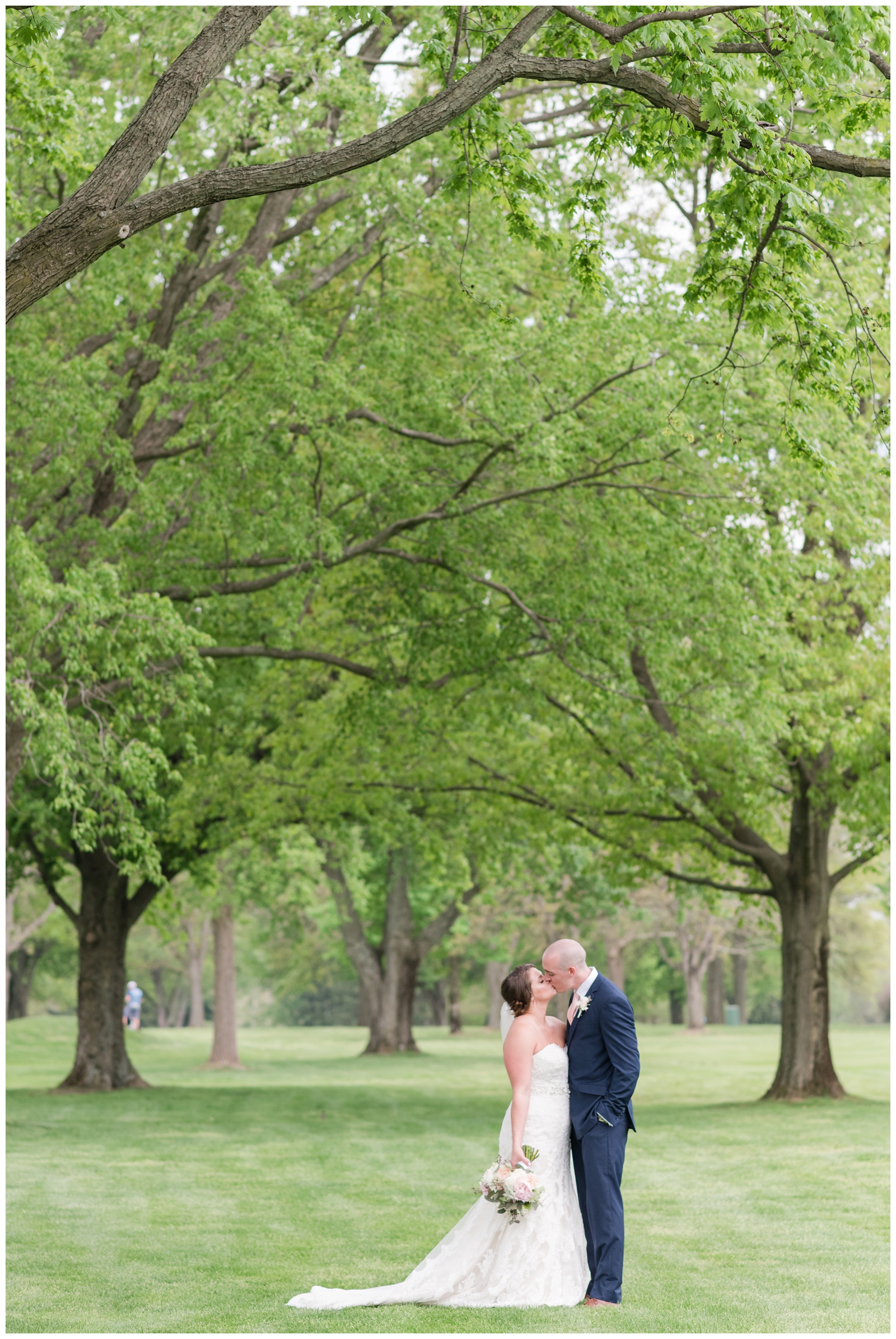 bride and groom kiss under the trees along Brookside Golf and Country Club green