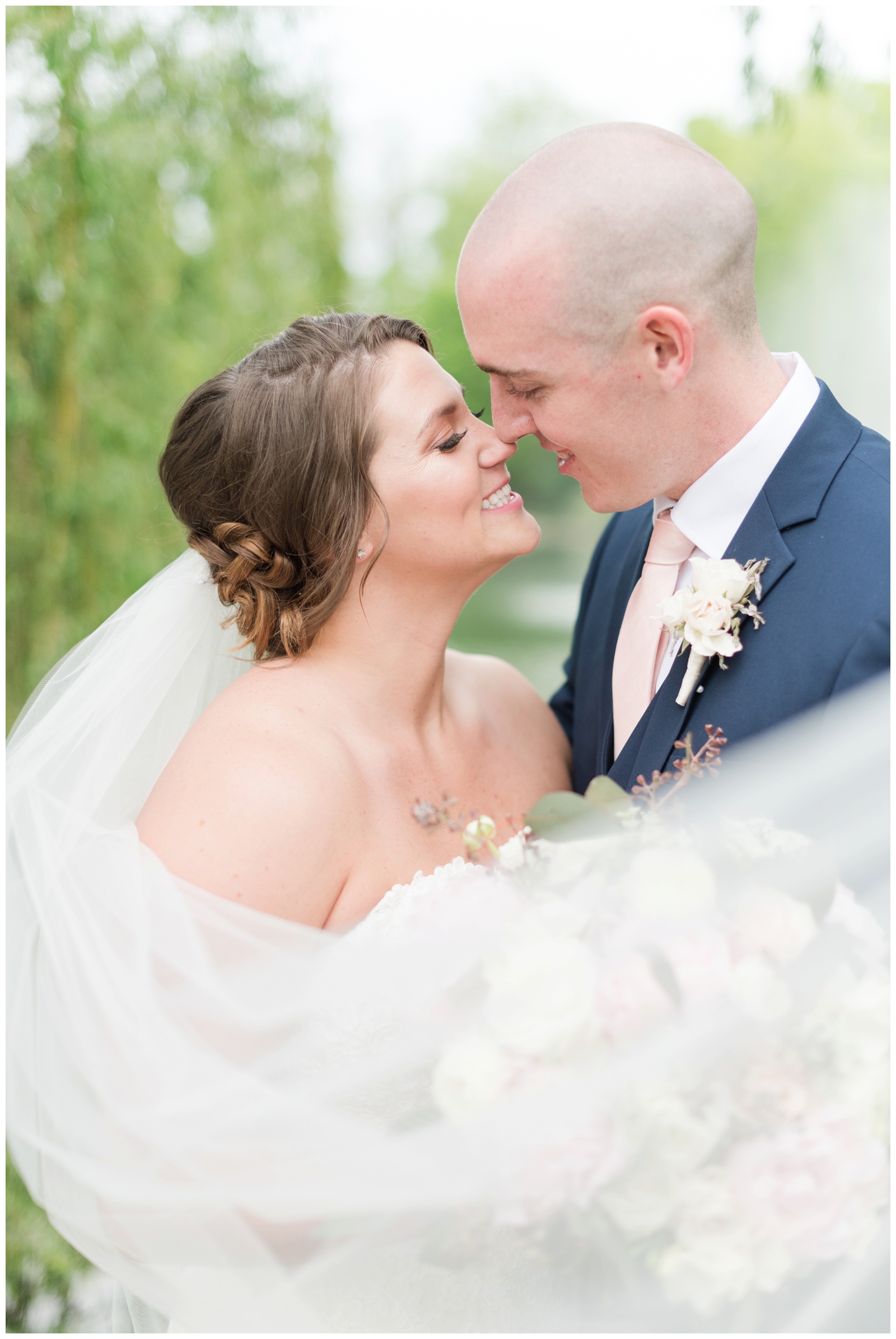 romantic wedding portrait of bride and groom nuzzling noses while her veil is draped around them