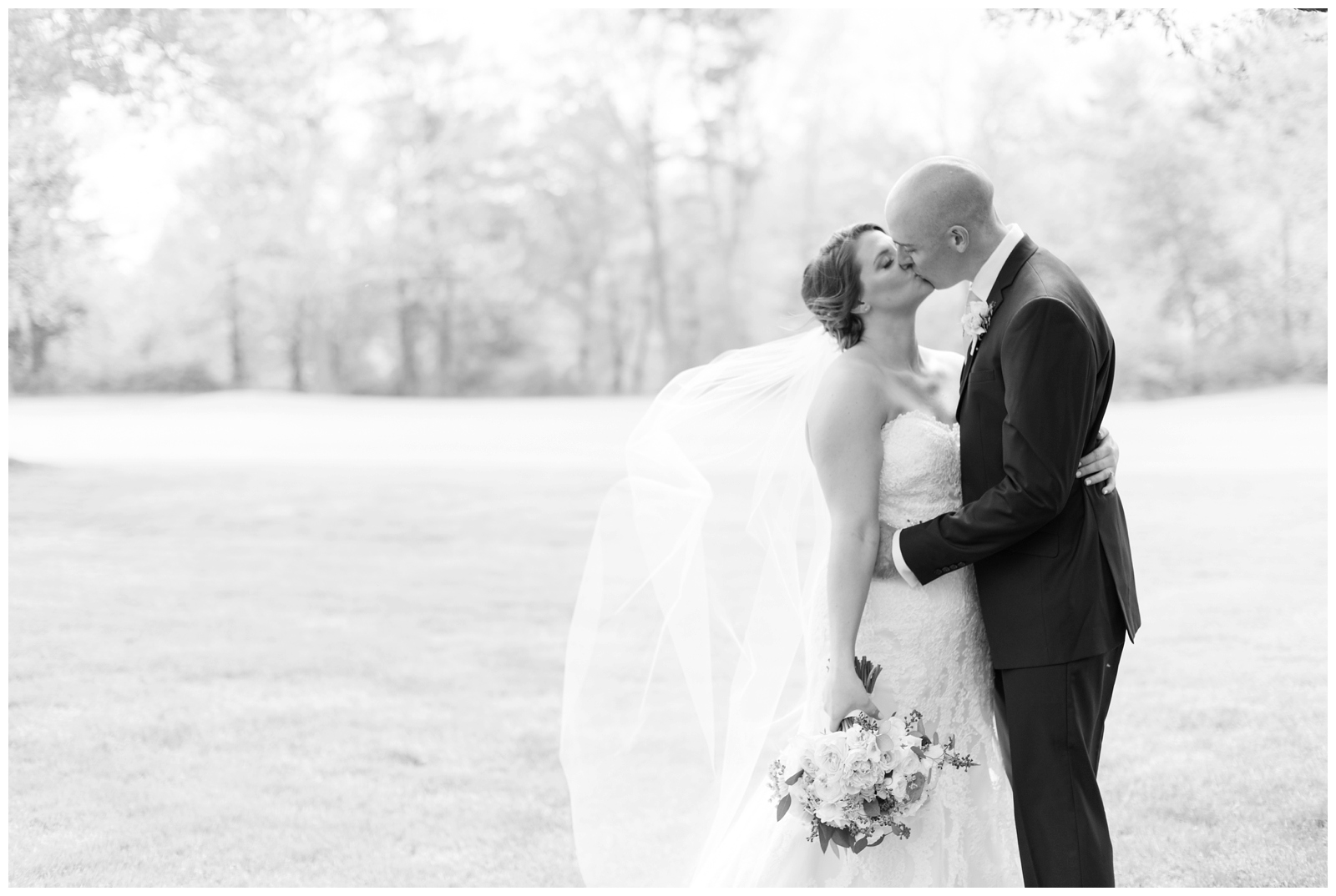 black and white portrait of bride and groom kissing while bride's veil blows in the wind