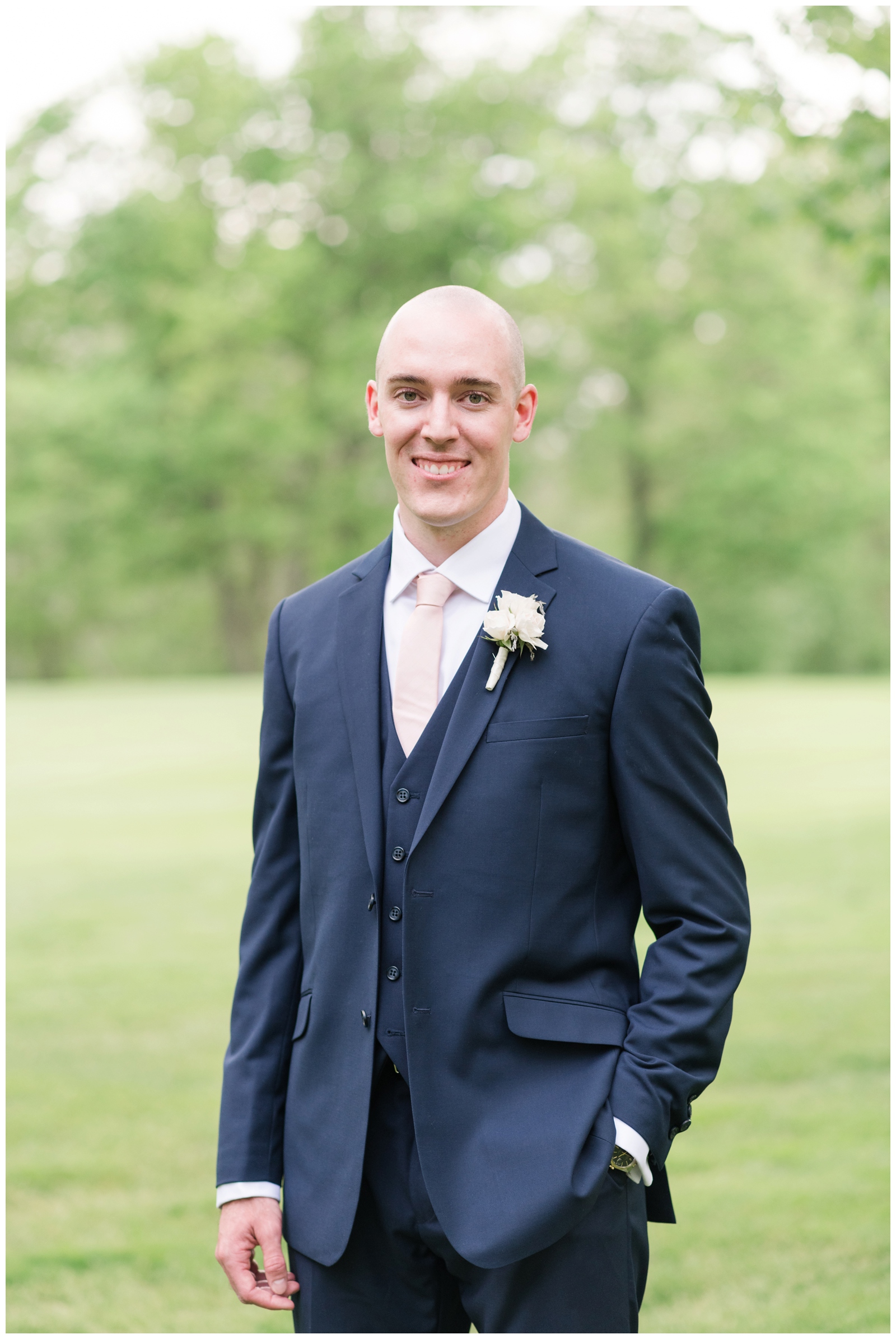 portrait of groom with one hand in pocket and navy suit with white boutonniere 