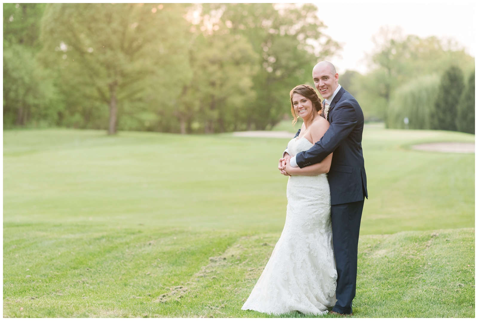 wedding portrait of bride and groom embracing on green of Brookside Golf and Country Club at sunset