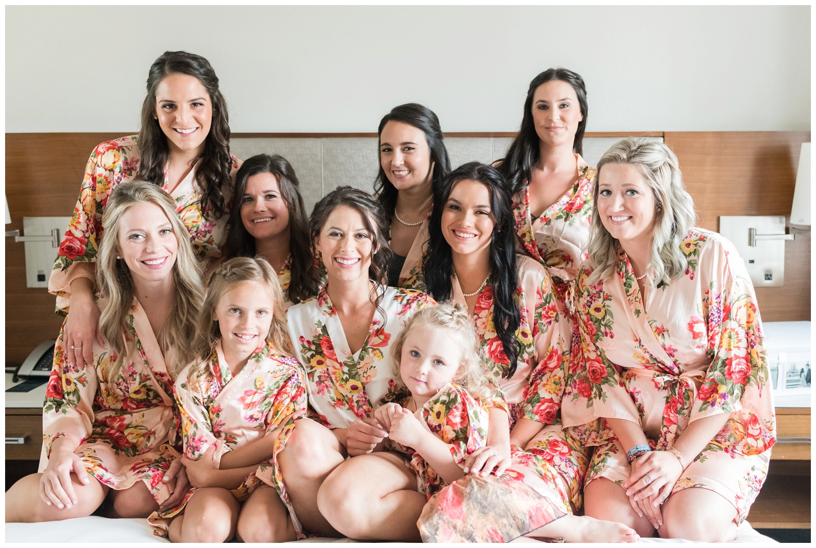 bride poses with bridesmaids in pale pink robes with two flower girls on bed before Ohio wedding