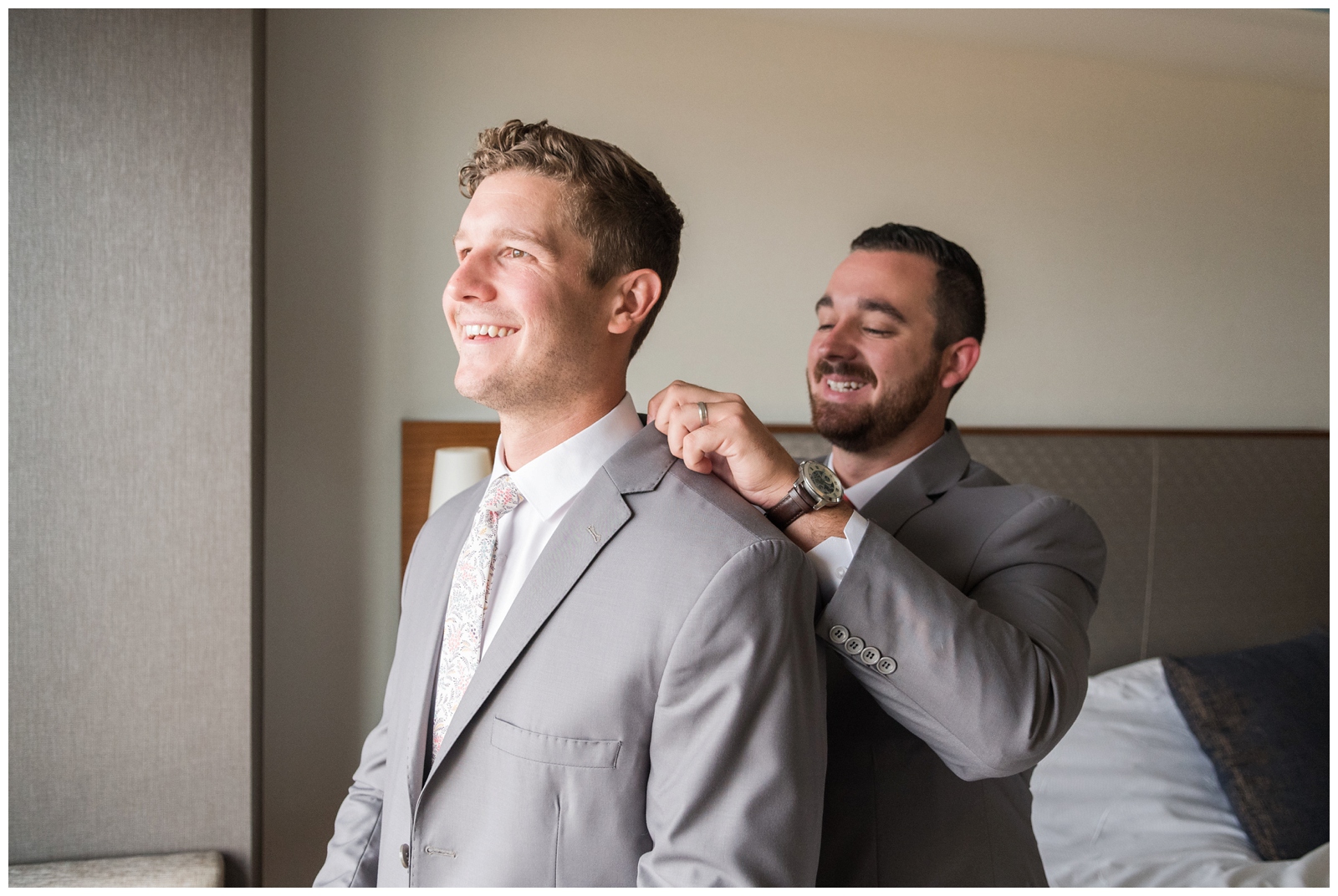 groomsman in grey suit helps groom adjust collar before Ohio wedding day