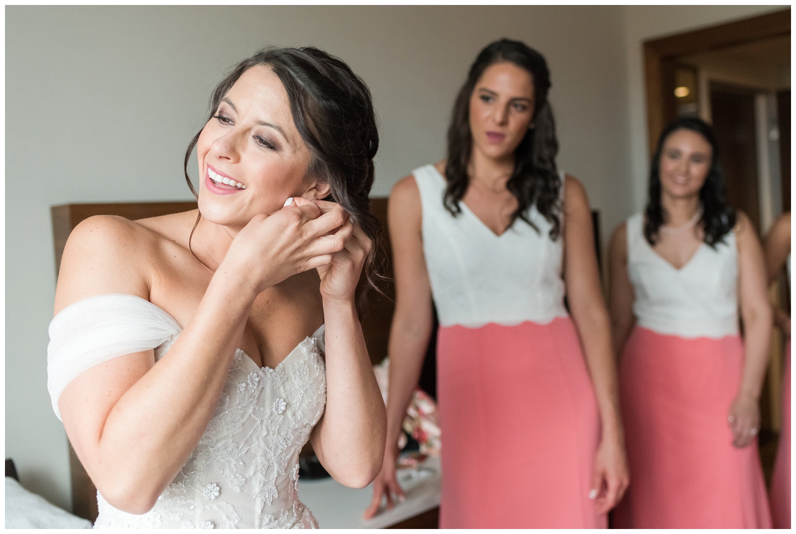 bride puts on earrings for wedding day in Columbus OH while bridesmaids in coral and white gowns watch
