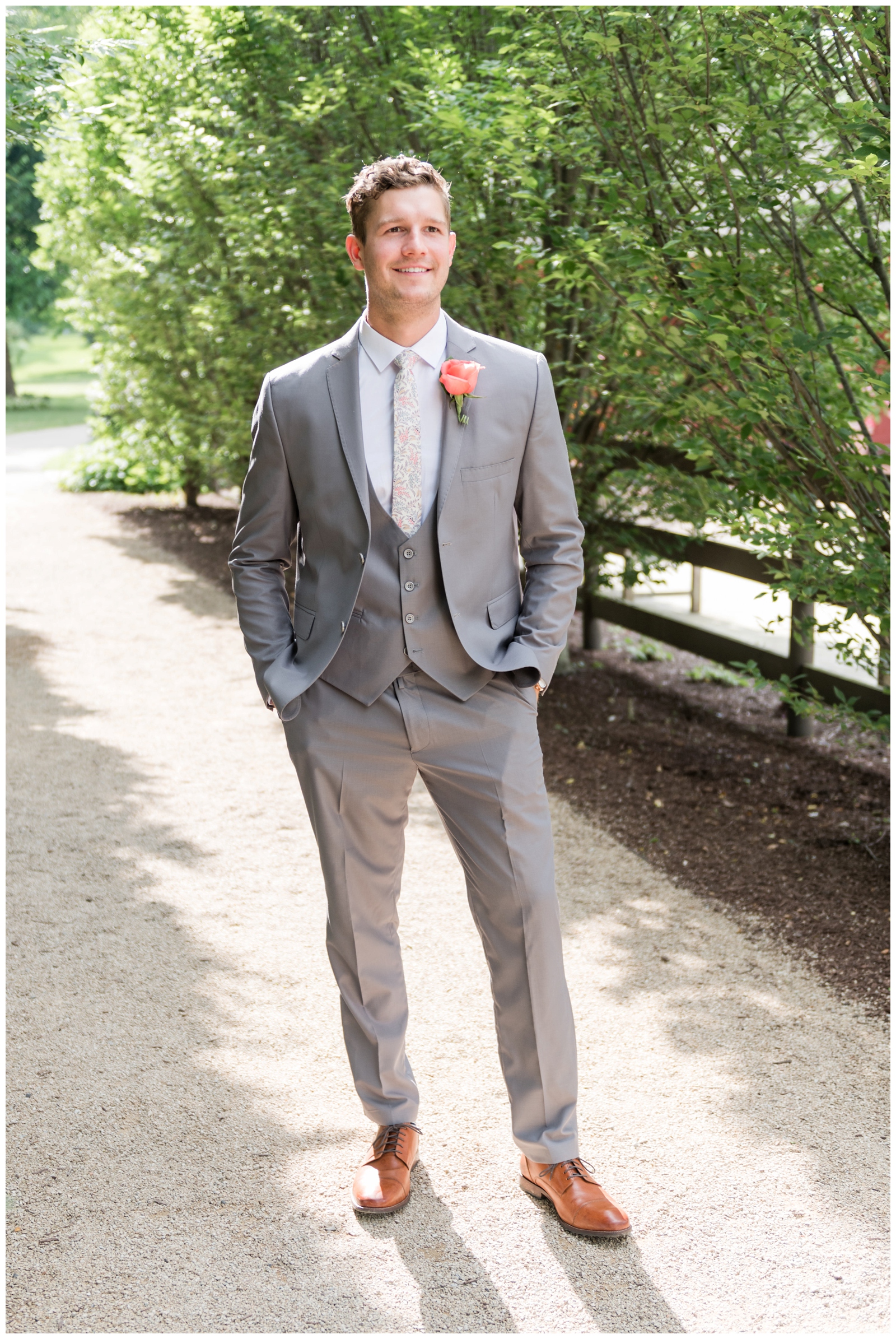 groom stands with his hands in his pockets of grey suit with coral boutonnière at Franklin Park Conservatory