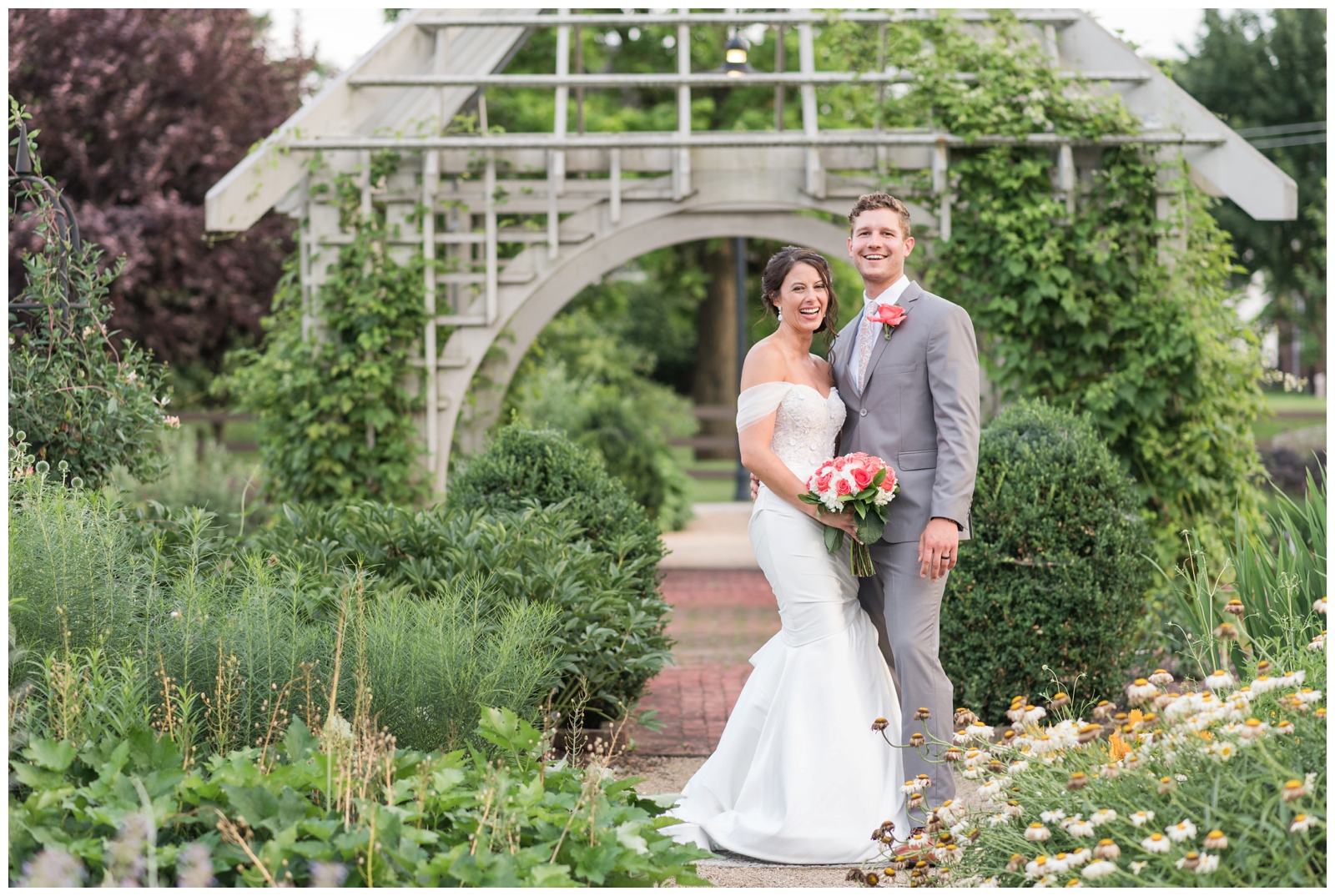 bride and groom pose in front of wooden structure in gardens of The Wells Barn