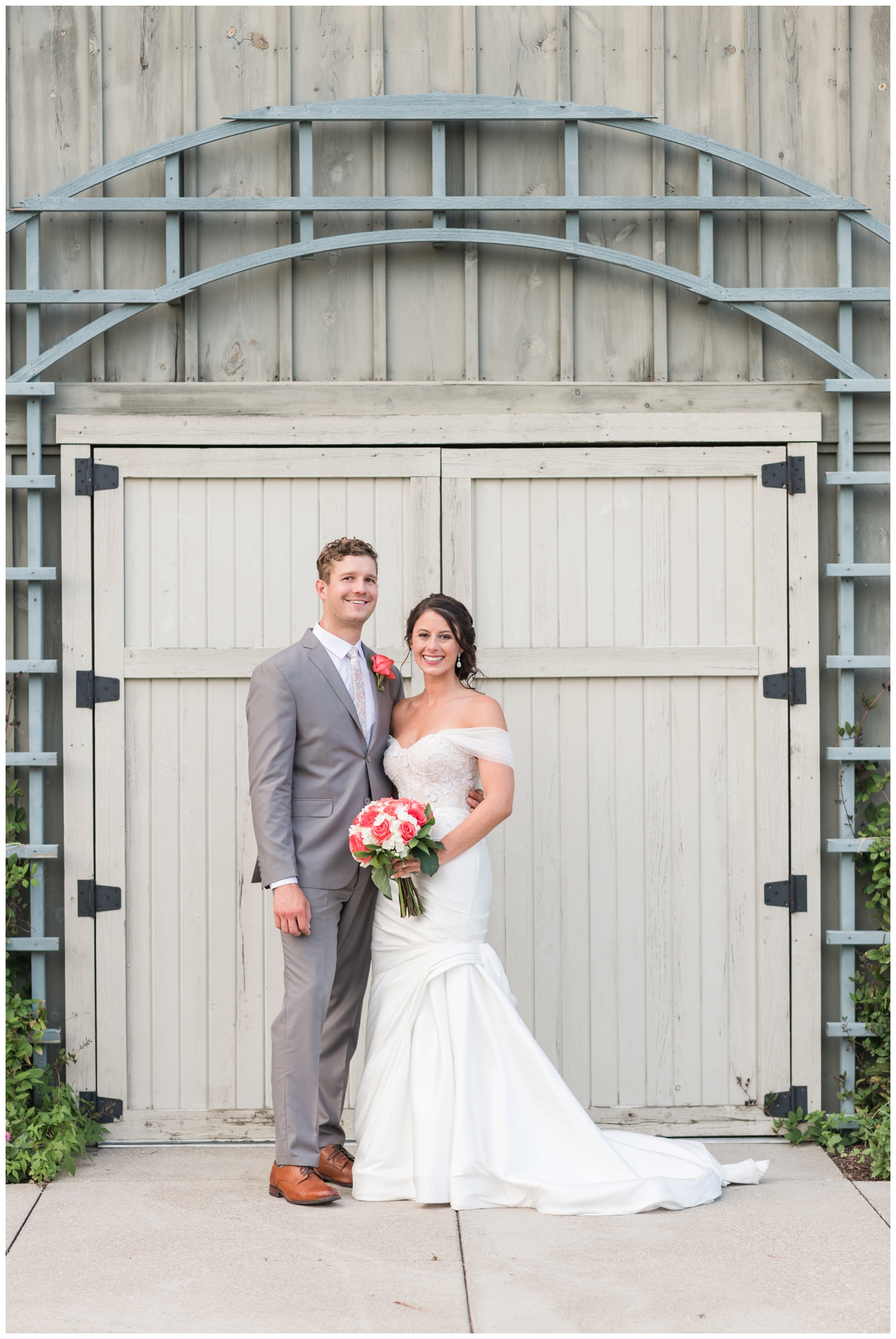 bride and groom stand in front of pale wood doors at The Wells Barn