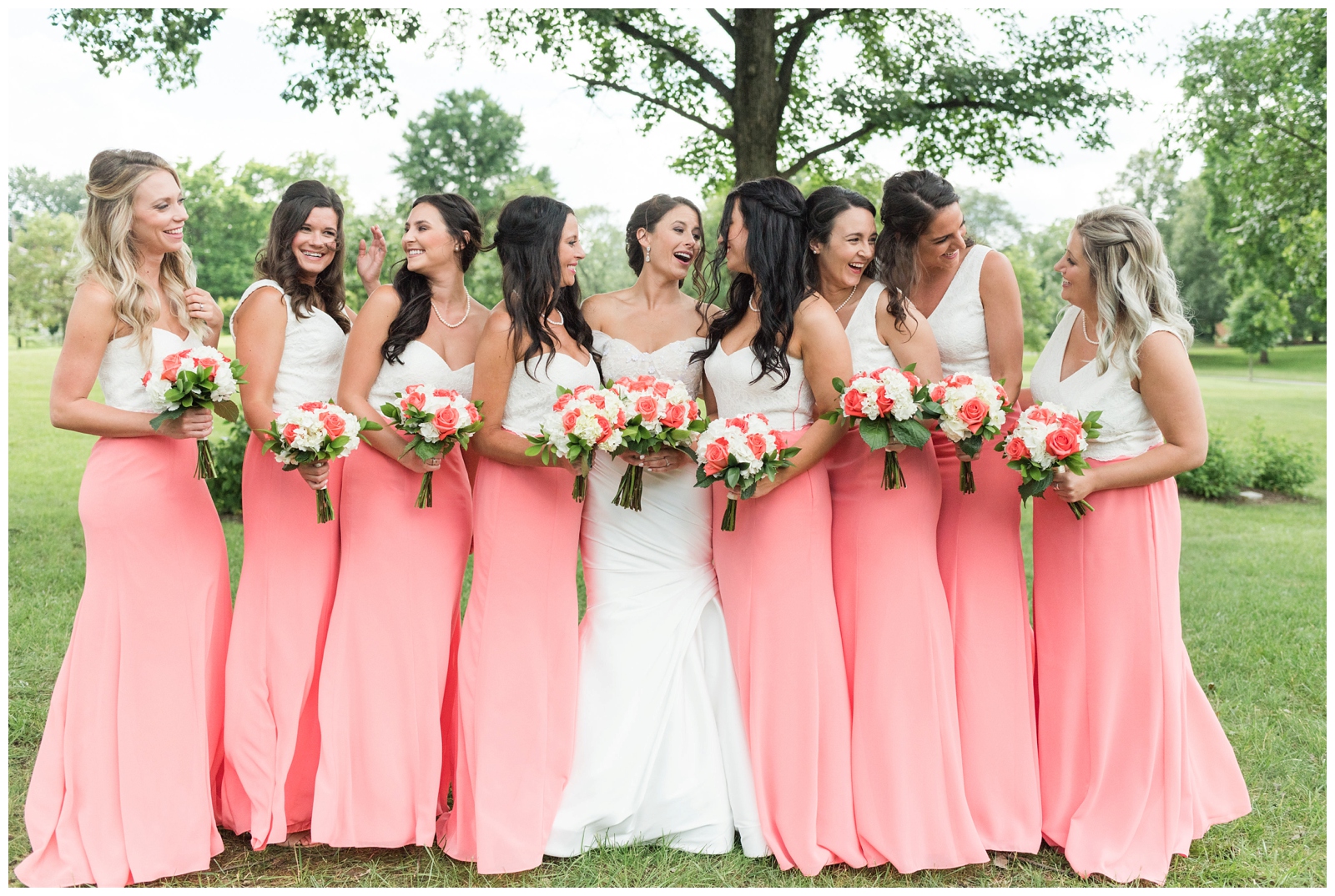 bride laughgs with seven bridesmaids in coral gowns with white tops before Ohio wedding day