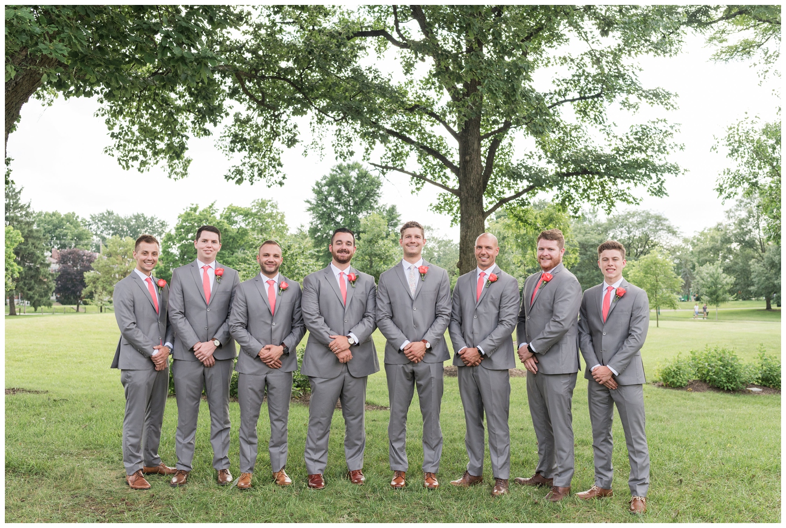 groom and groomsmen in grey suits with coral ties and boutonnières stand with hands crossed at The Wells Barn