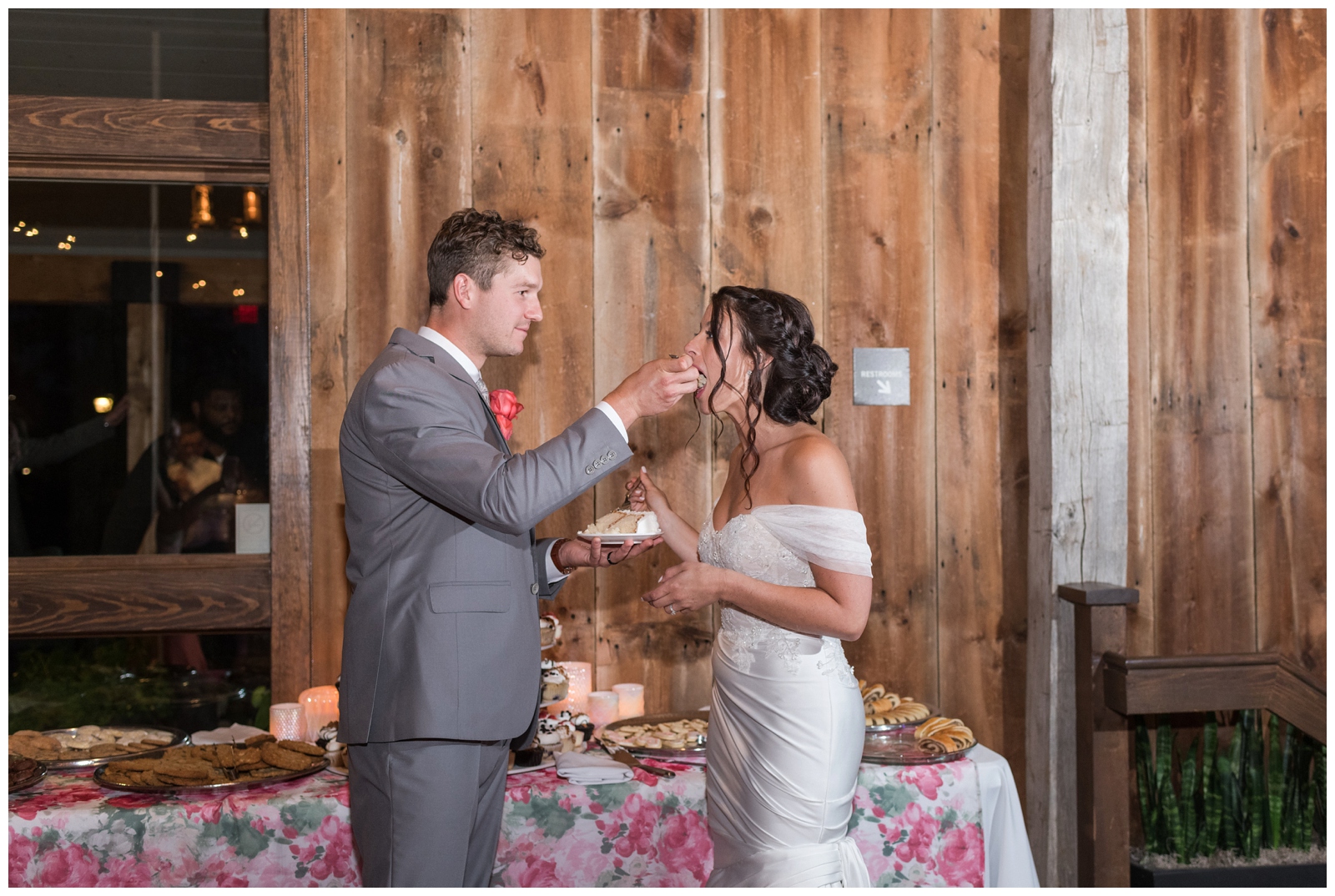 groom feeds bride a bite of wedding cake during reception at The Wells Barn