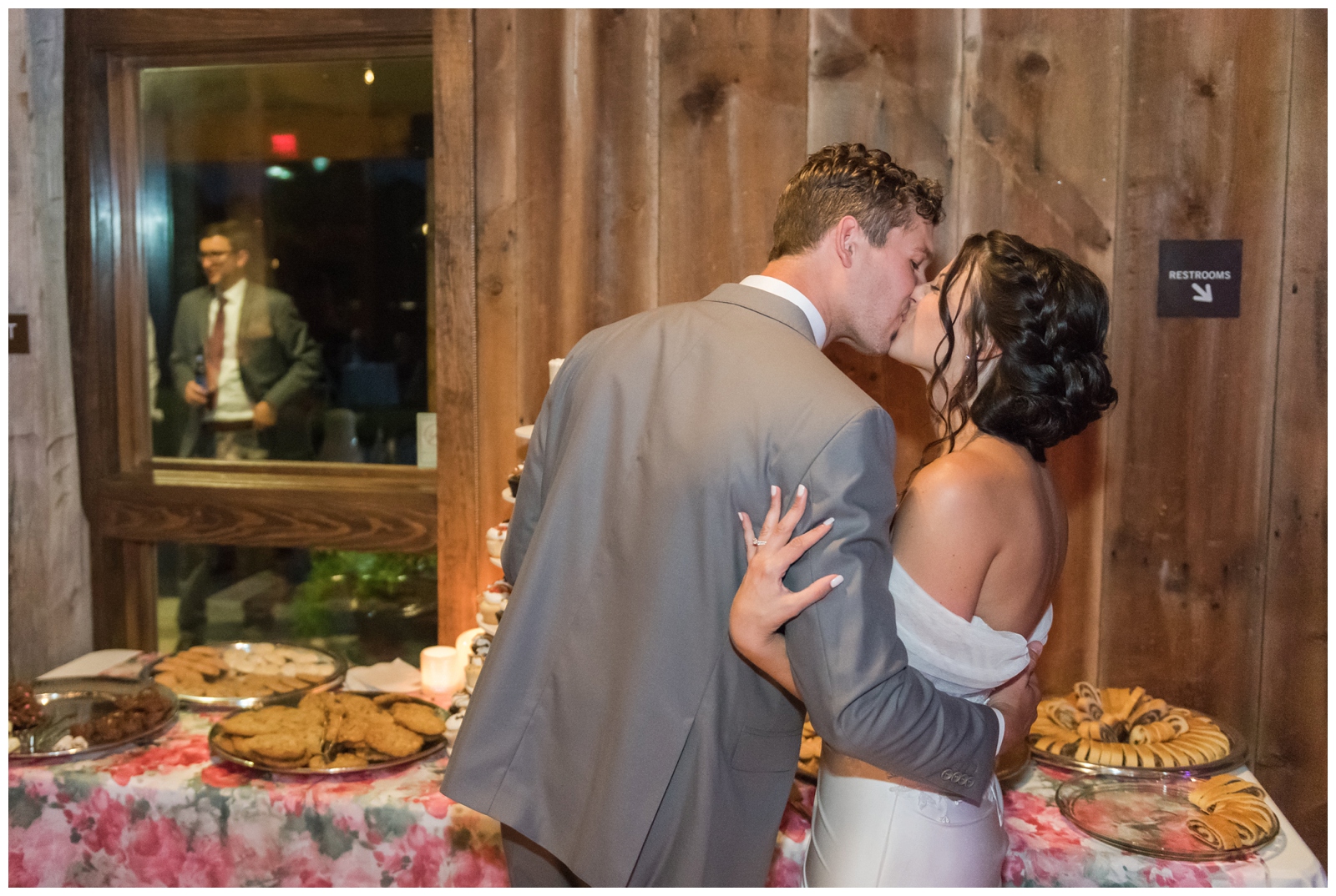 bride and groom kiss by dessert table during wedding at The Wells Barn