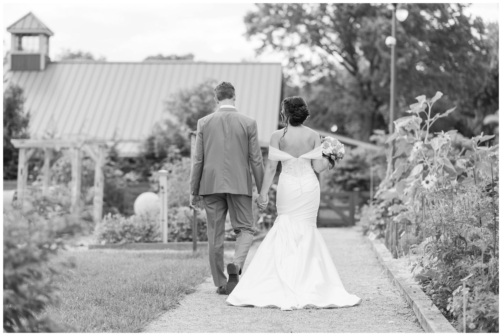 black and white portrait of bride and groom holding hands and walking in gardens of The Wells Barn