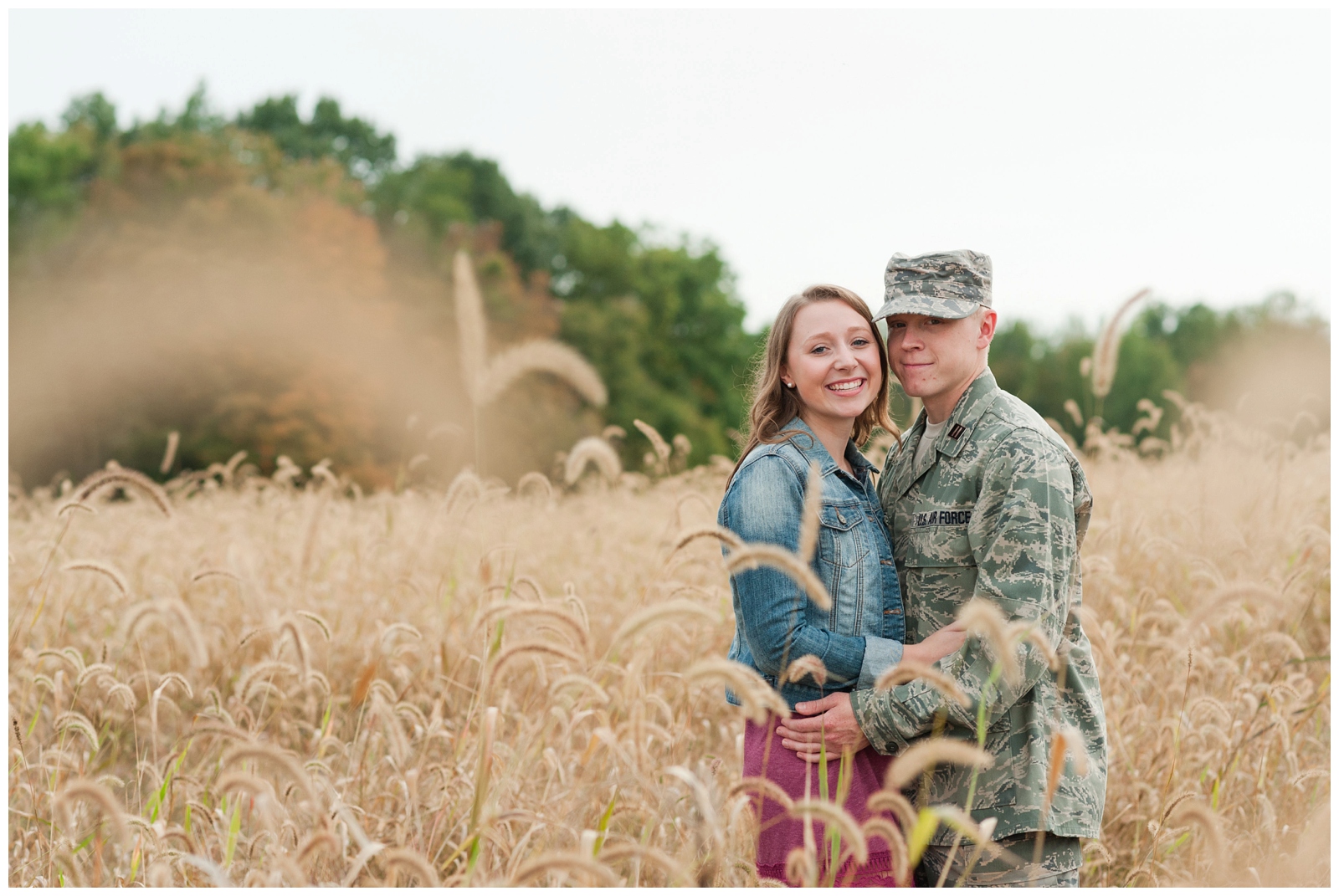 Engaged couple looking at camera in wheat field with burgundy dress and military bdus on in Country Engagement Session Sunbury Ohio