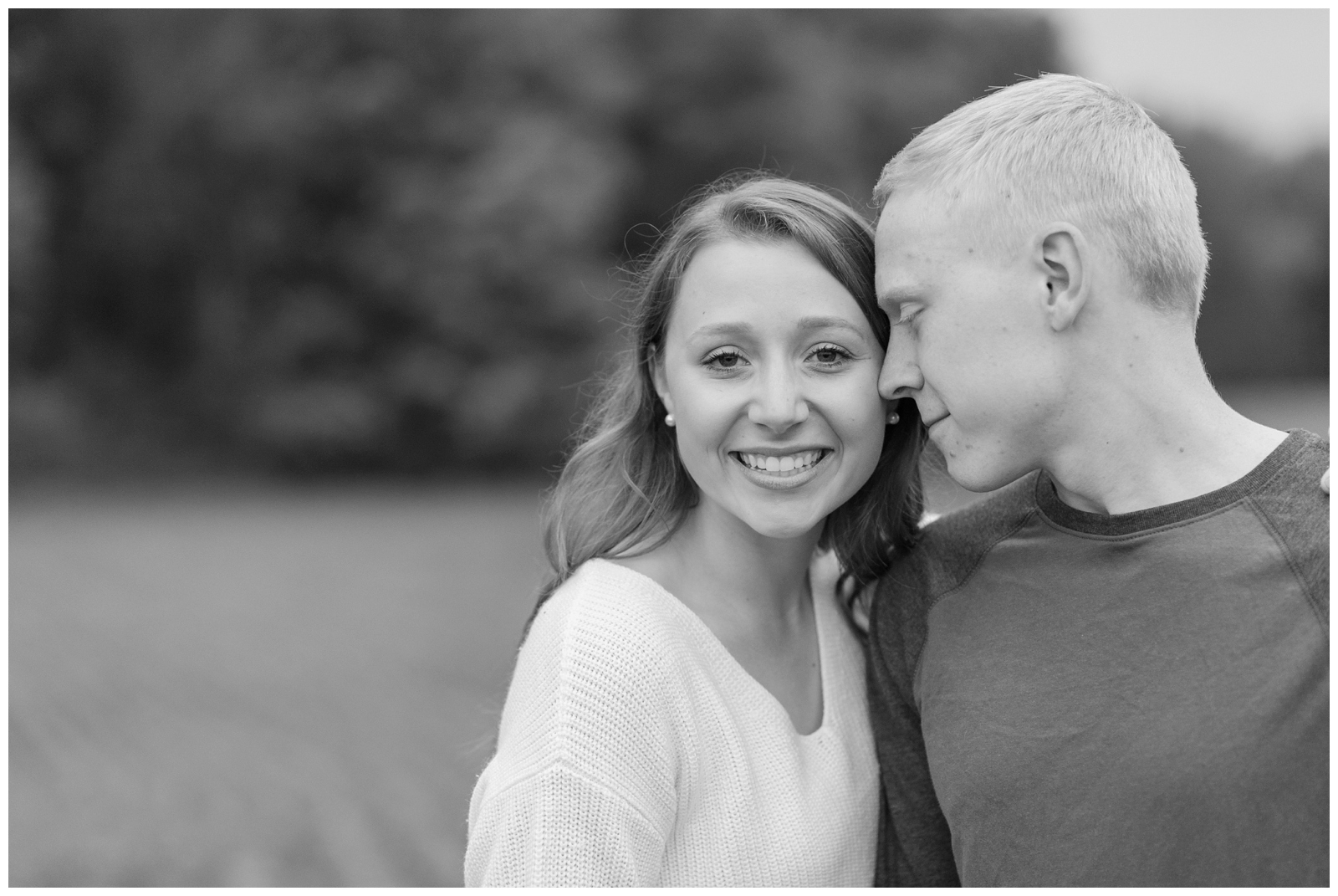 black and white photo of engaged girl smiling at camera with engaged man looking at her 