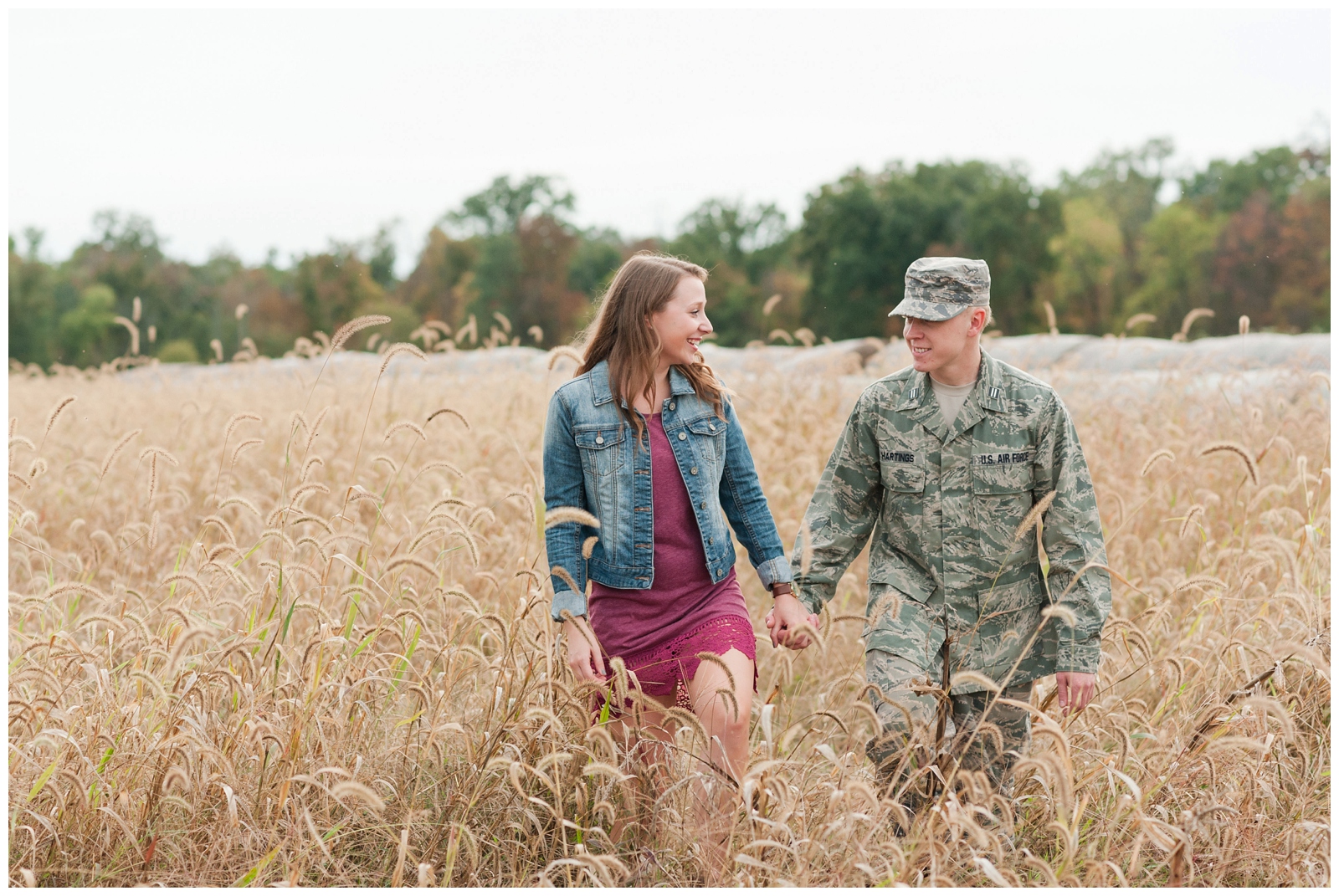 engaged couple happily smiling at each other while walking through wheat field during their autumn engagement session in sunbury ohio by pipers photography 