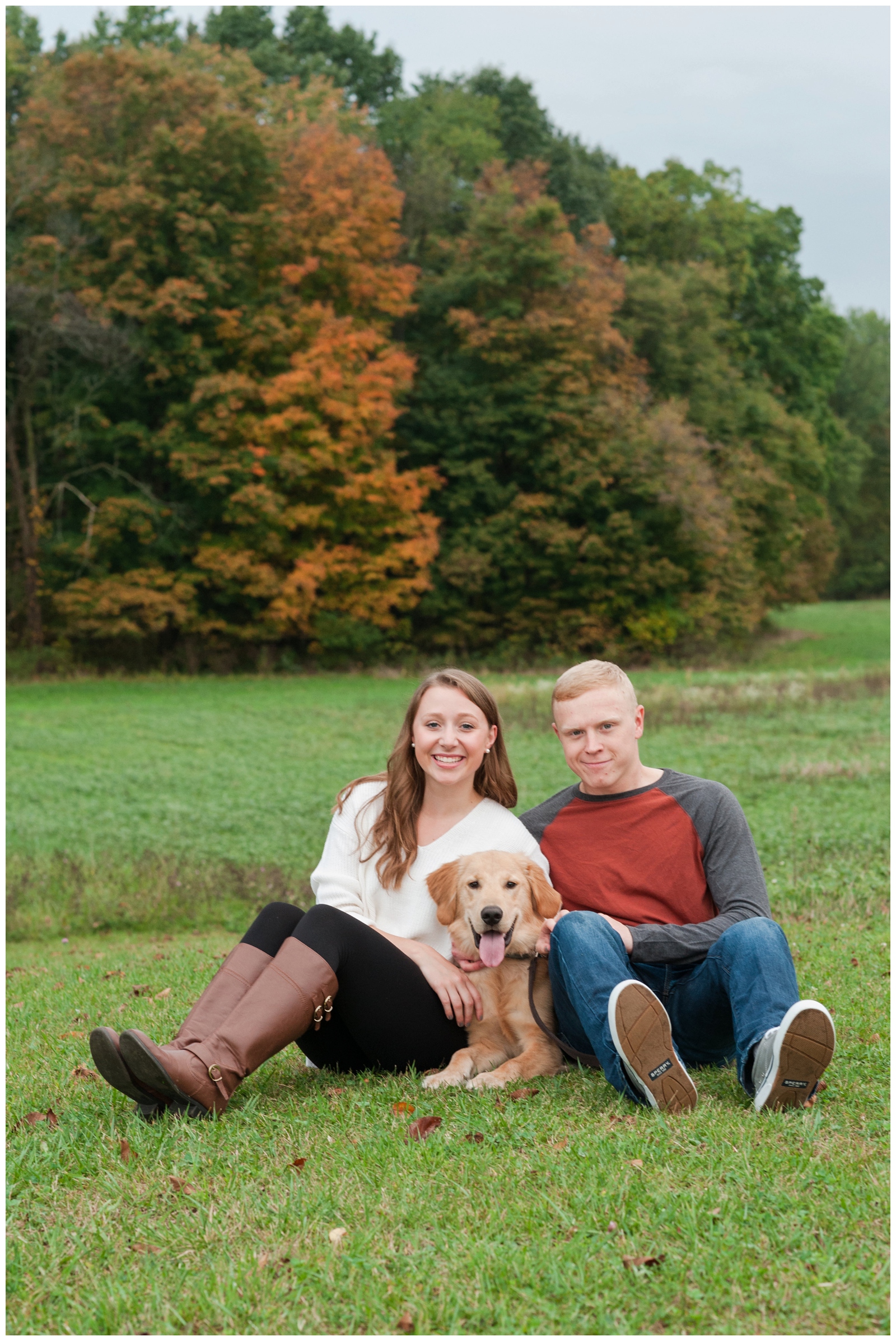 couple sitting in the grass with their dog during couple happily laughing and smiling while casually walking through wheat field during their country engagement session in sunbury ohio 