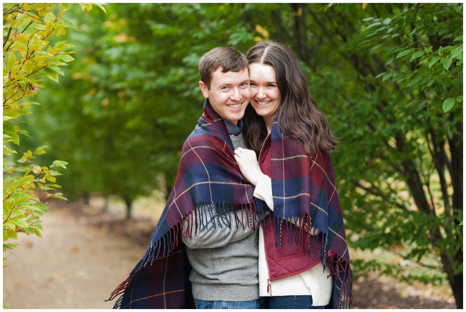 engaged couple laughing at the camera happily wrapped in a blanket 