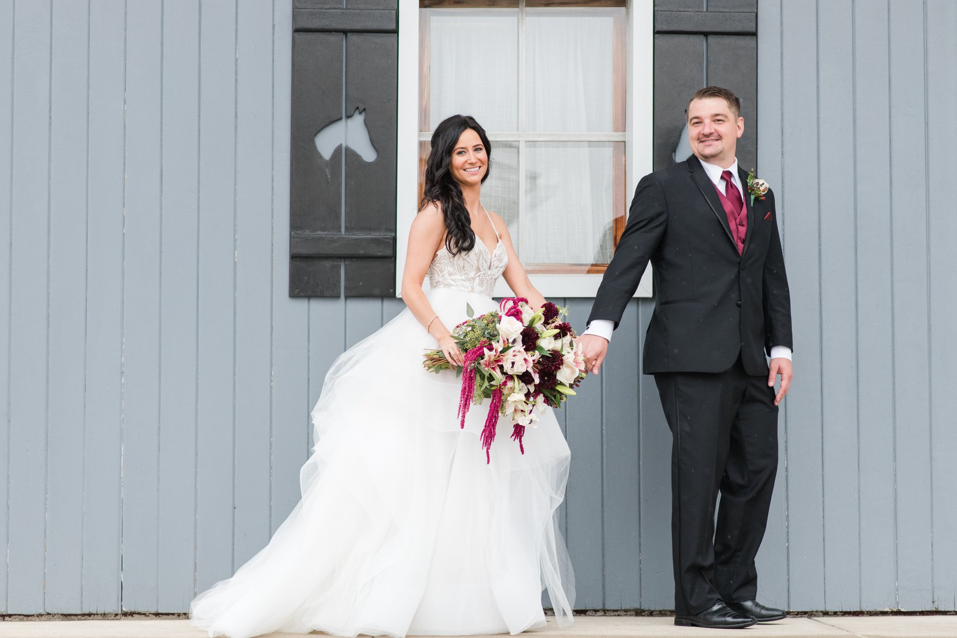 bride and groom walking in front of a blue building on their wedding at smiling at the camera at brookside farms in louisville ohio 