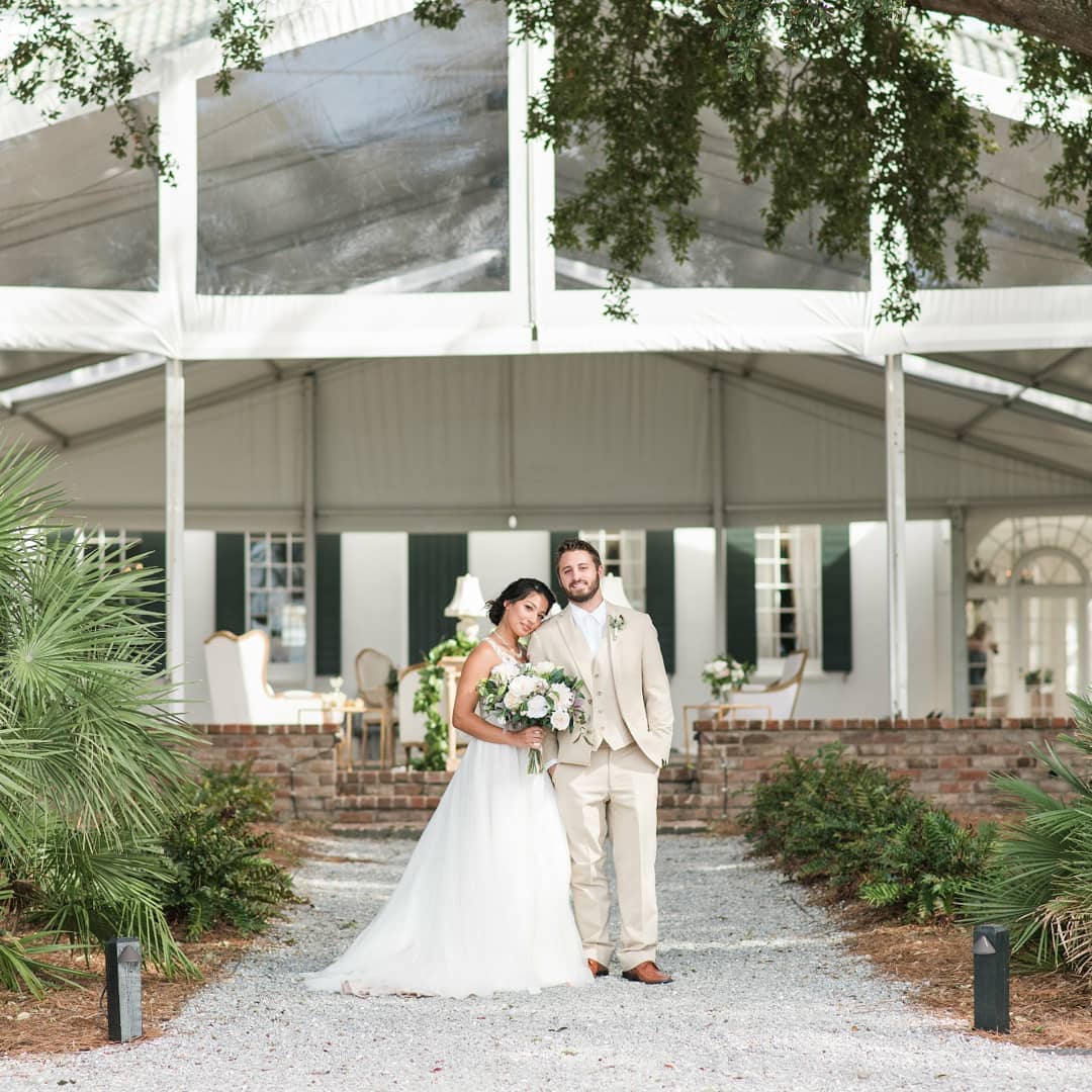bride and groom smiling at the camera together in front of their venue at lowndes grove plantation in charleston, south carolina 