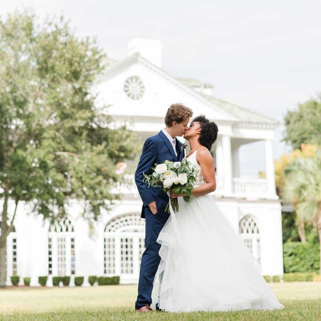 bride and groom kissing in front of their wedding venue in charleston, south carolina. Lowndes Grove plantation wedding photos 