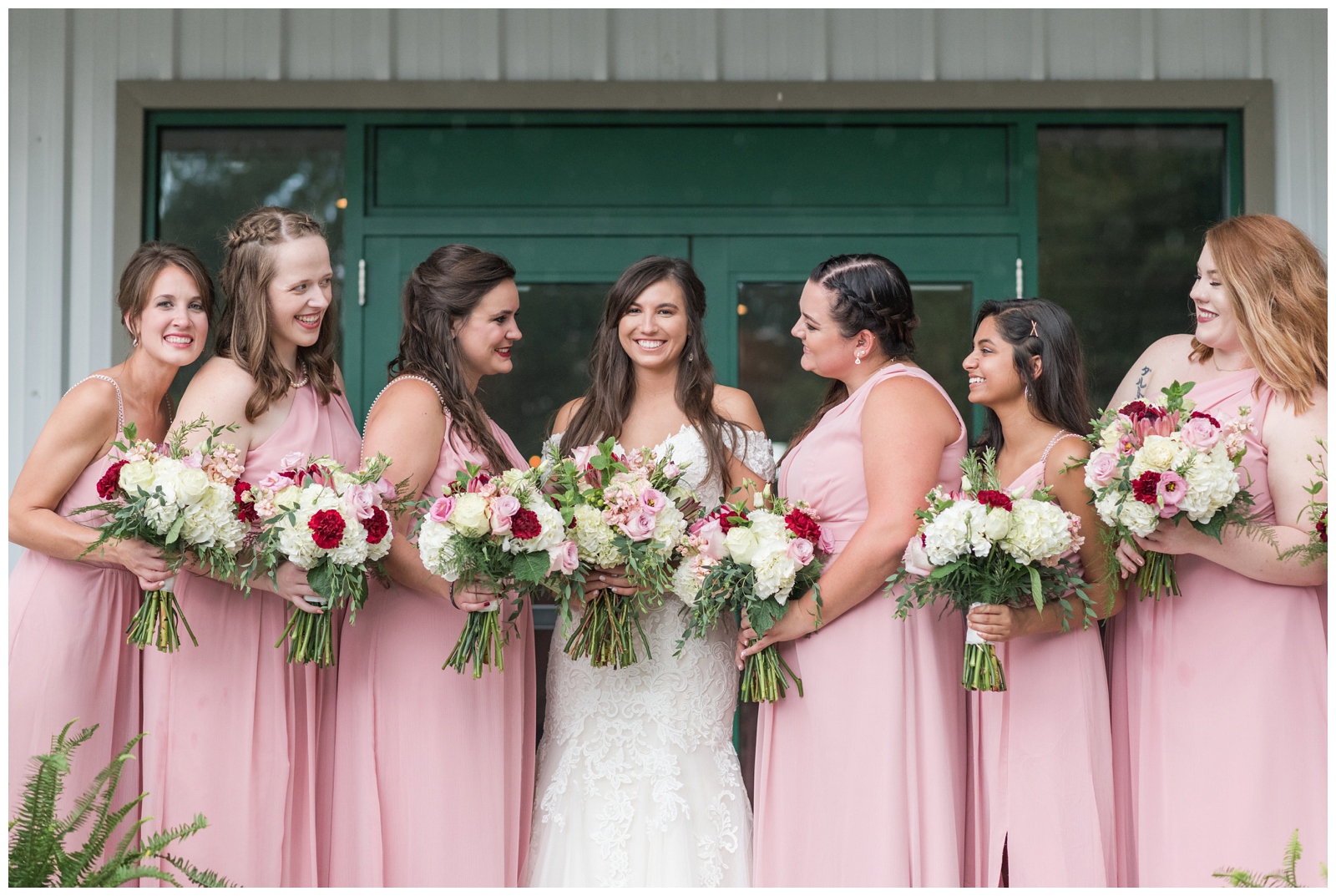 bridesmaids in blush pink dresses looking at laughing with each other holding their bouquets at irongate equestrian center with bride 