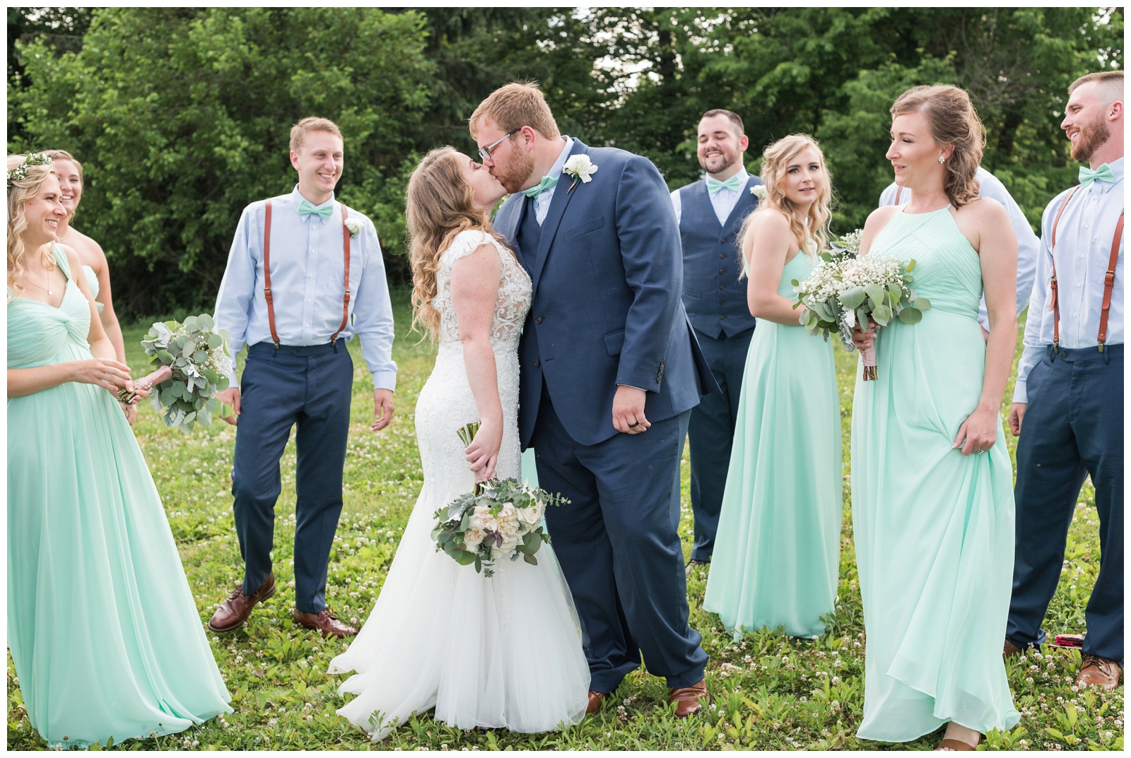groom kisses bride with bridal party in mint gowns around them