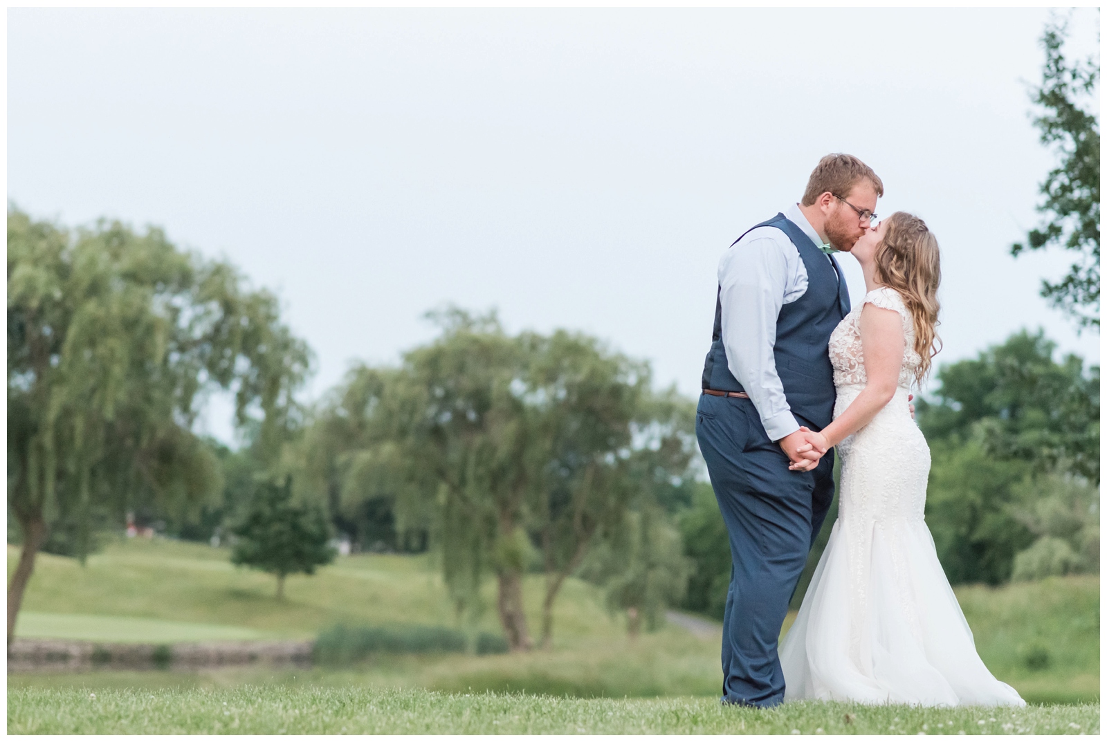 bride and groom hold hands kissing in front of lake at EagleSticks Golf Club