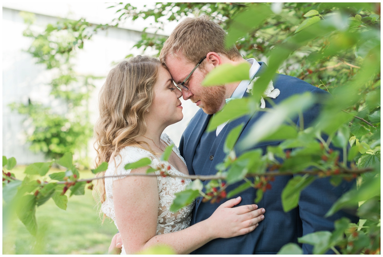 bride and groom touch noses while posing between trees at EagleSticks Golf Club