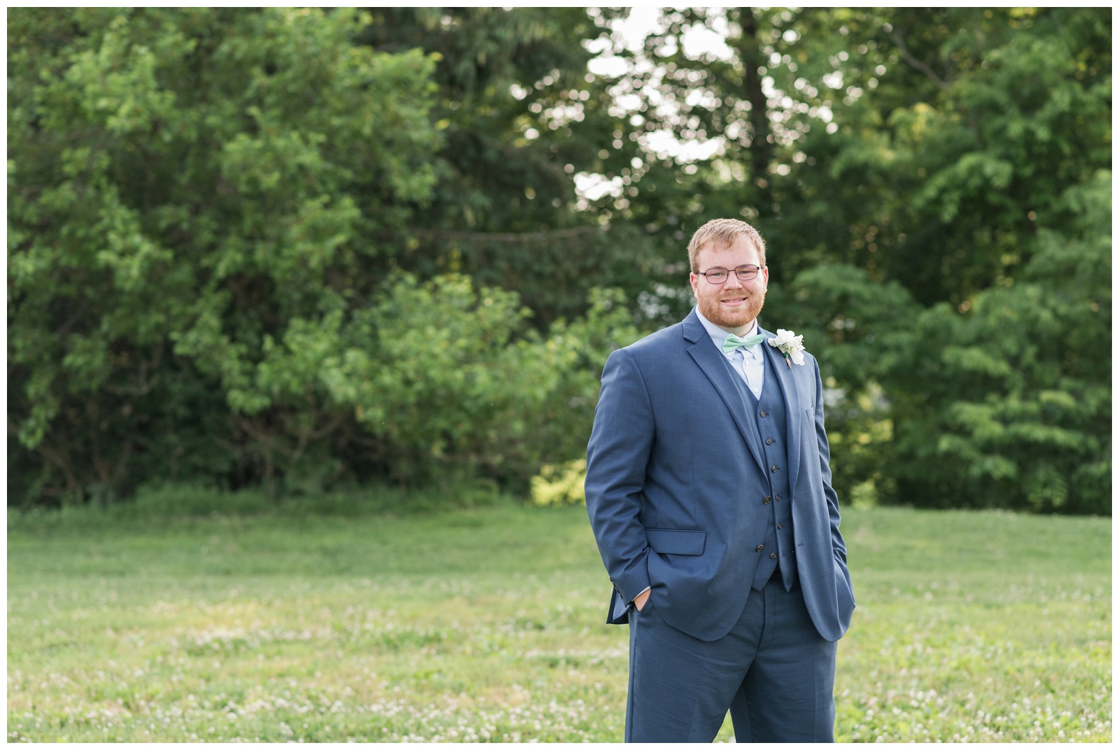 groom in navy suit with mint tie stands with his hands in pockets on OH golf course