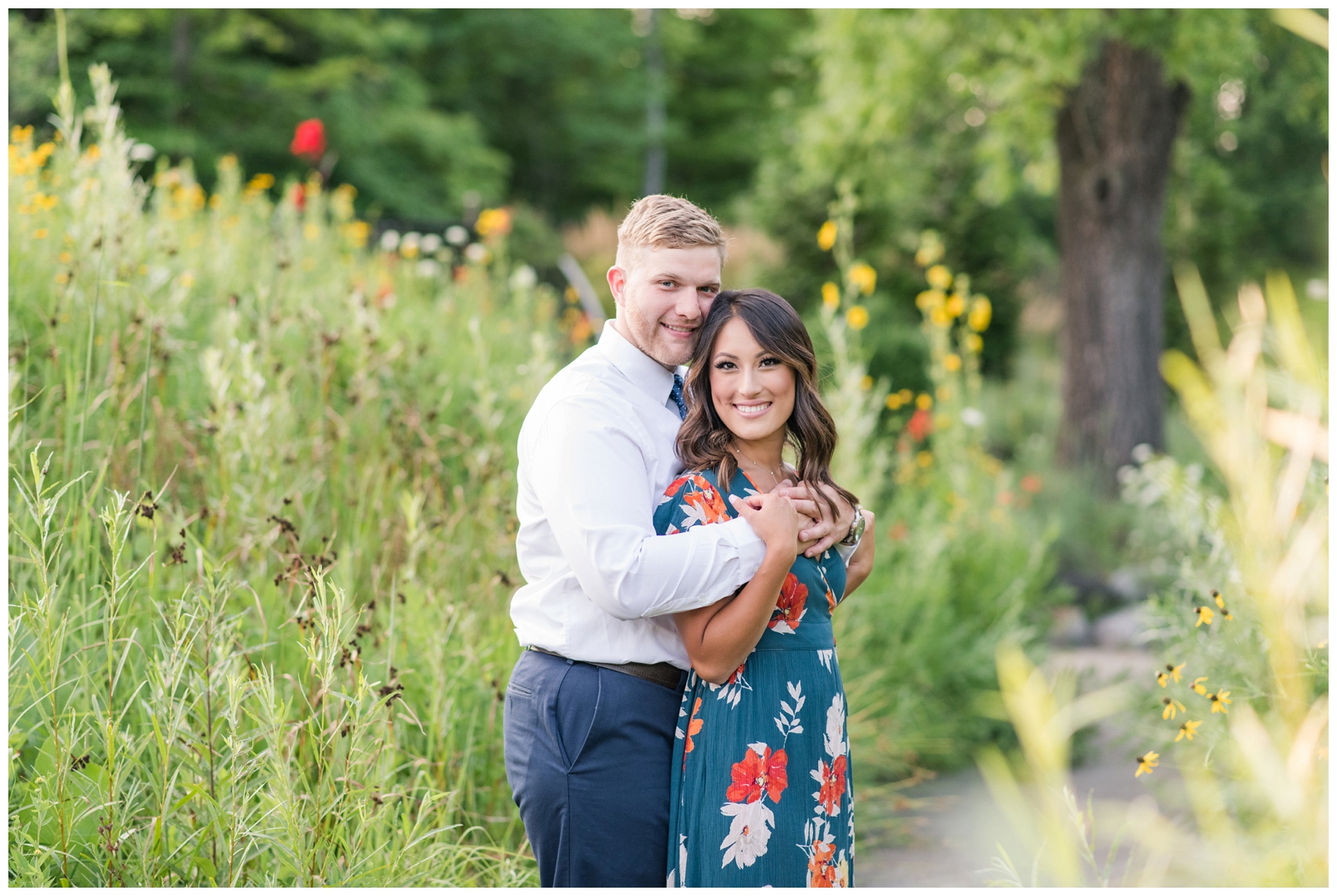 engaged couple smiling at the camera in the center of the image with garden greens surrounding them 