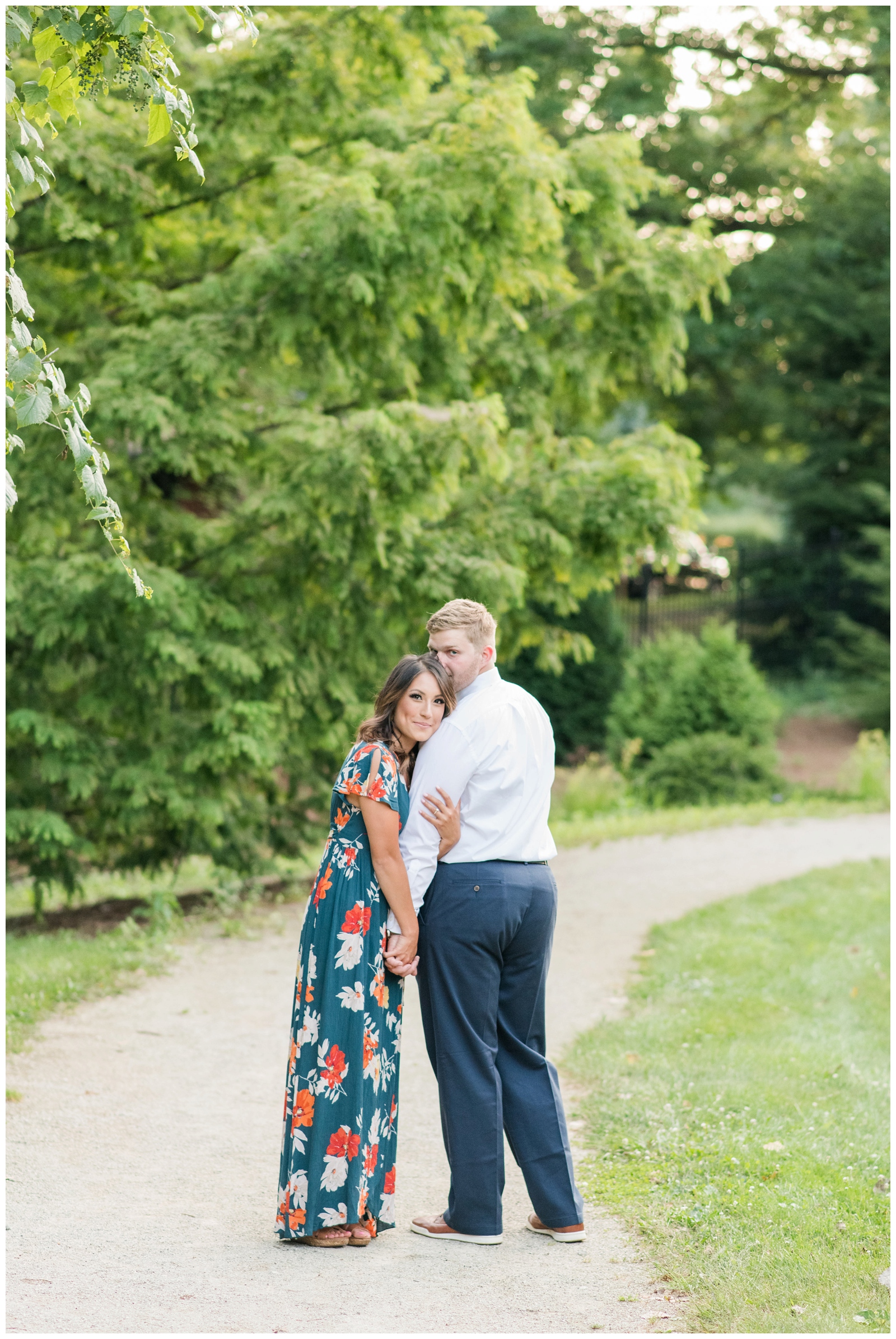 couple smiling at the camera while standing on a dirt road during summer engagement session at inniswood metro garden 