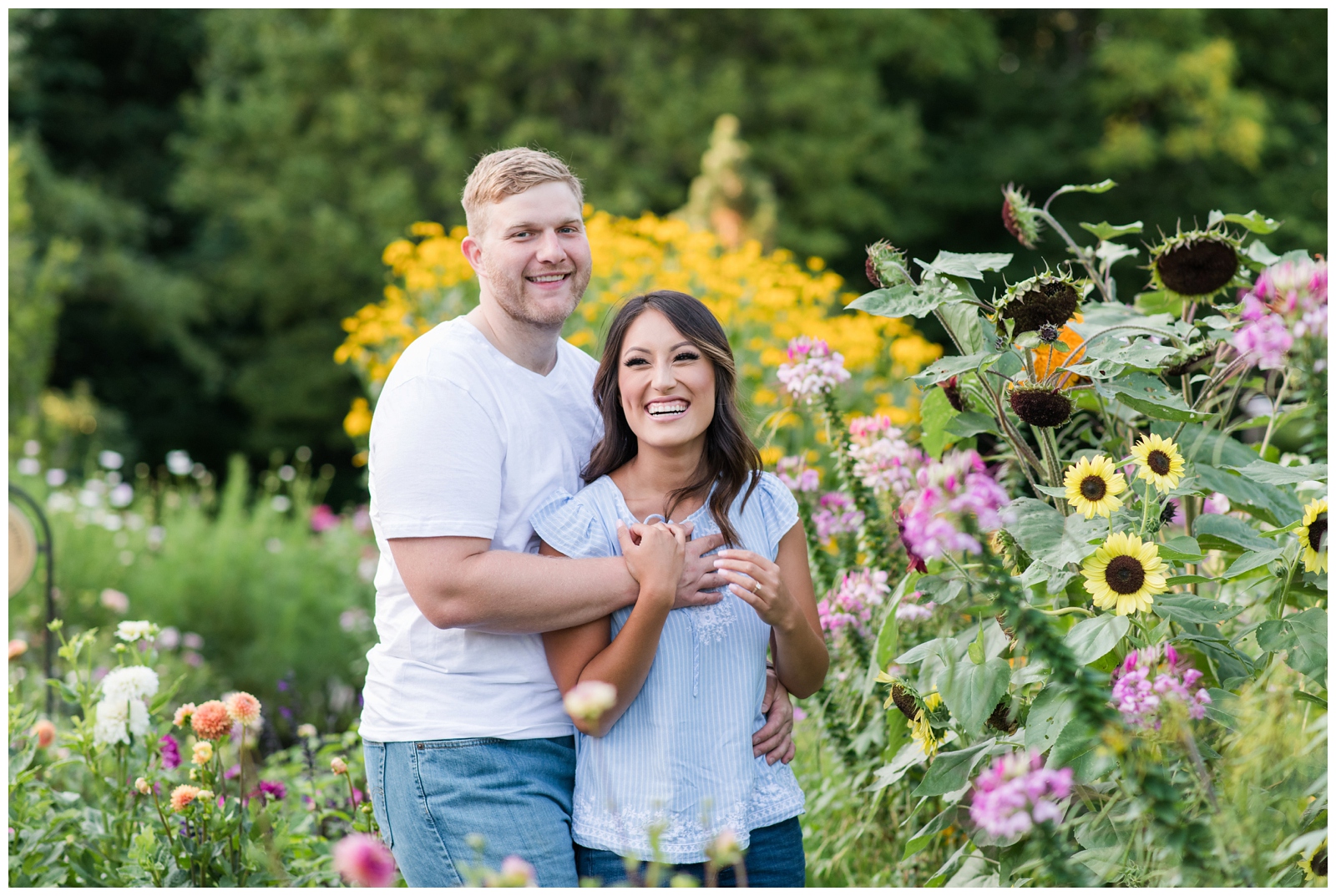 engaged couple happily looking at the camera surrounded by flowers in a garden 