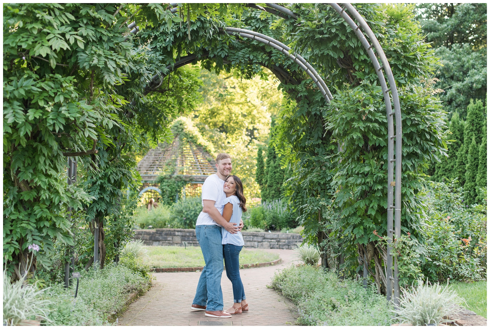man and women laughing and hugging during their engagement session surrounded by a leafy green arbor in their casual wear at Inniswood metro gardens Engagement Session
