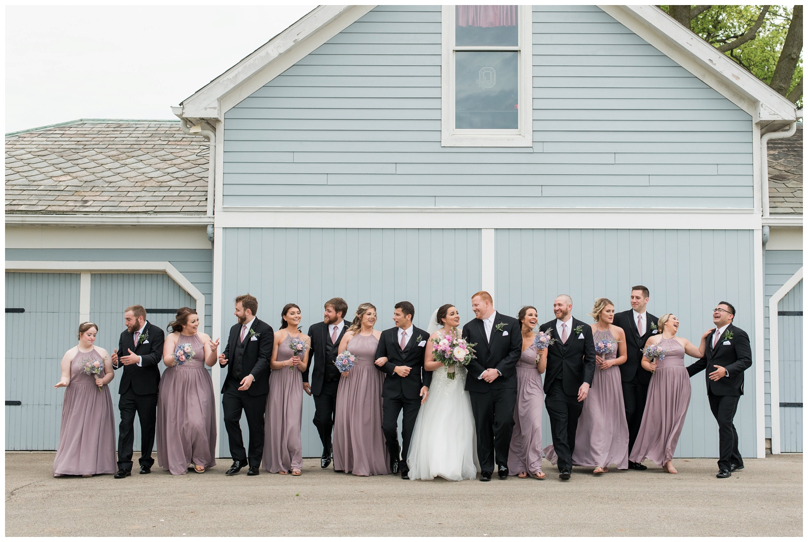 bridal party in pink and black pose by blue wall at Pretty Prairie Farms