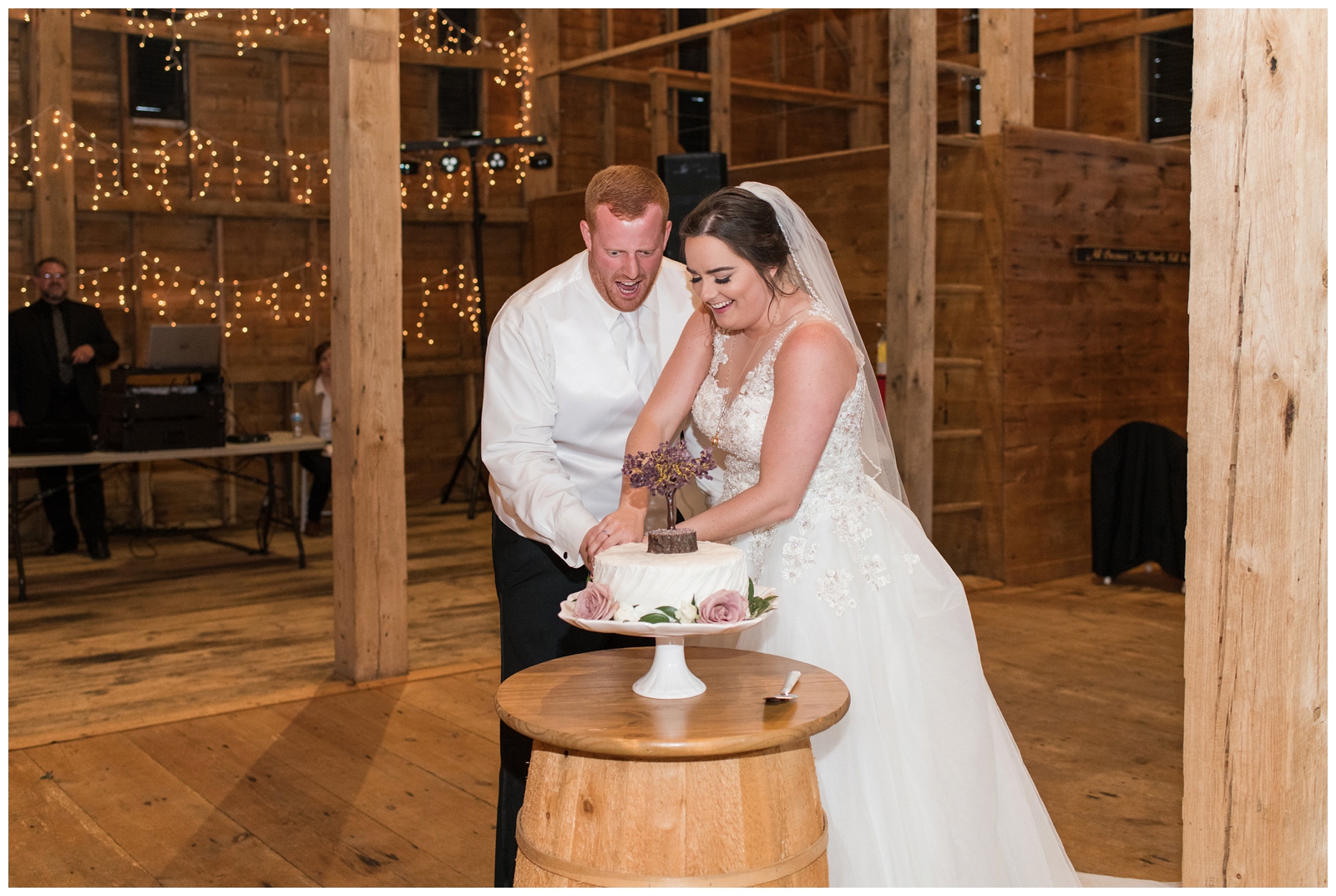 Bride and groom cut single layer wedding cake on barrel during barn reception at Pretty Prairie Farms