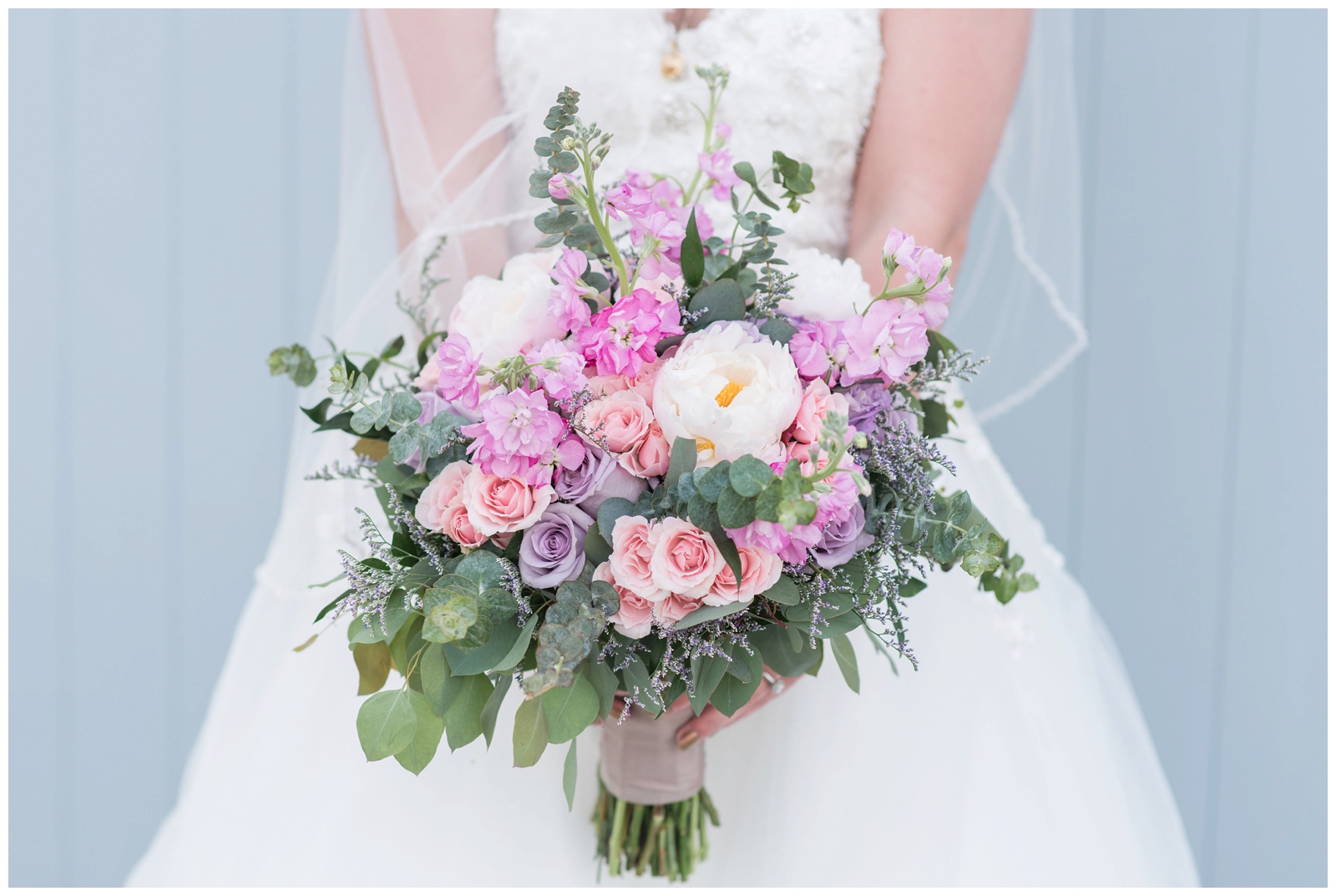spring wedding bouquet with white peonies, purple and pink roses held by bride in lace gown