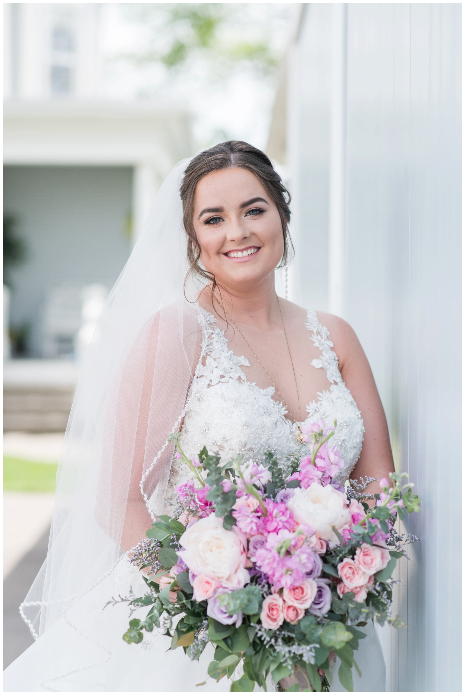 bride smiles in lace wedding gown with pink and purple wedding bouquet poses for bridal portrait at Pretty Prairie Farms