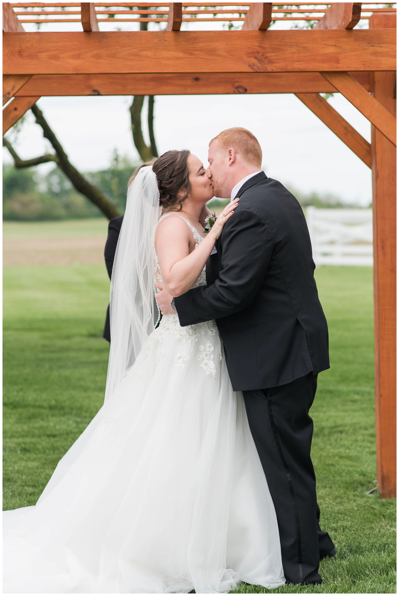 first kiss as husband and wife under wooden arbor at Pretty Prairie Farms