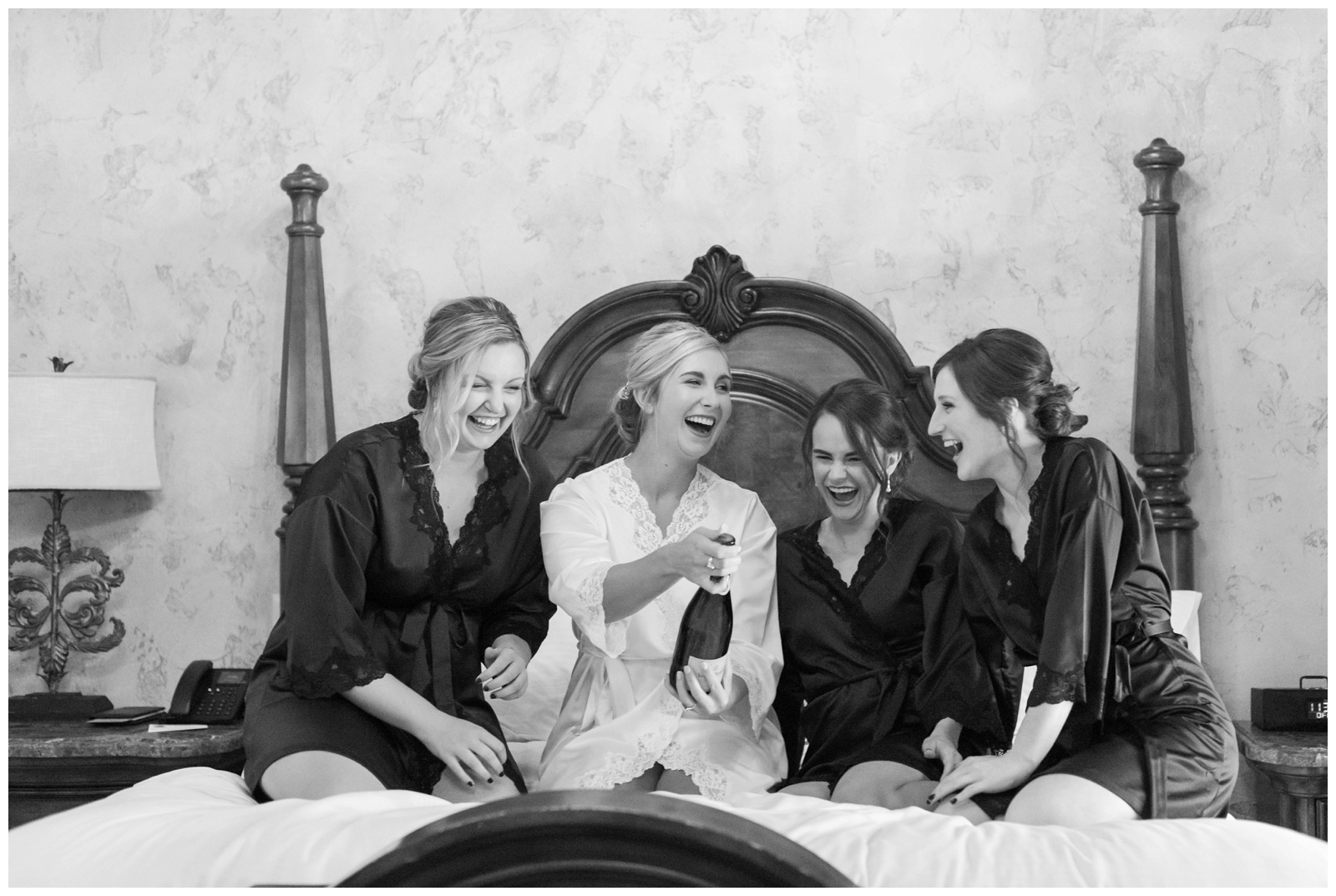 bride pops champagne on bed with three bridesmaids preparing for Canton OH wedding
